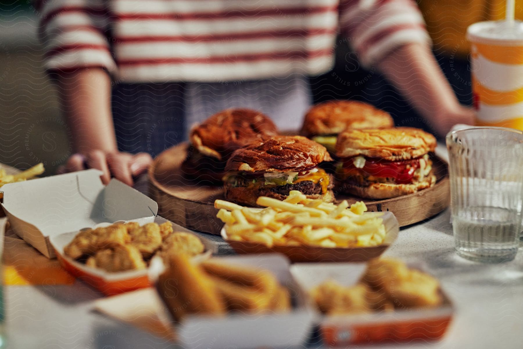 A person standing with hands at the edge of a table overlooking a tray filled with burgers and chicken nuggets with fries