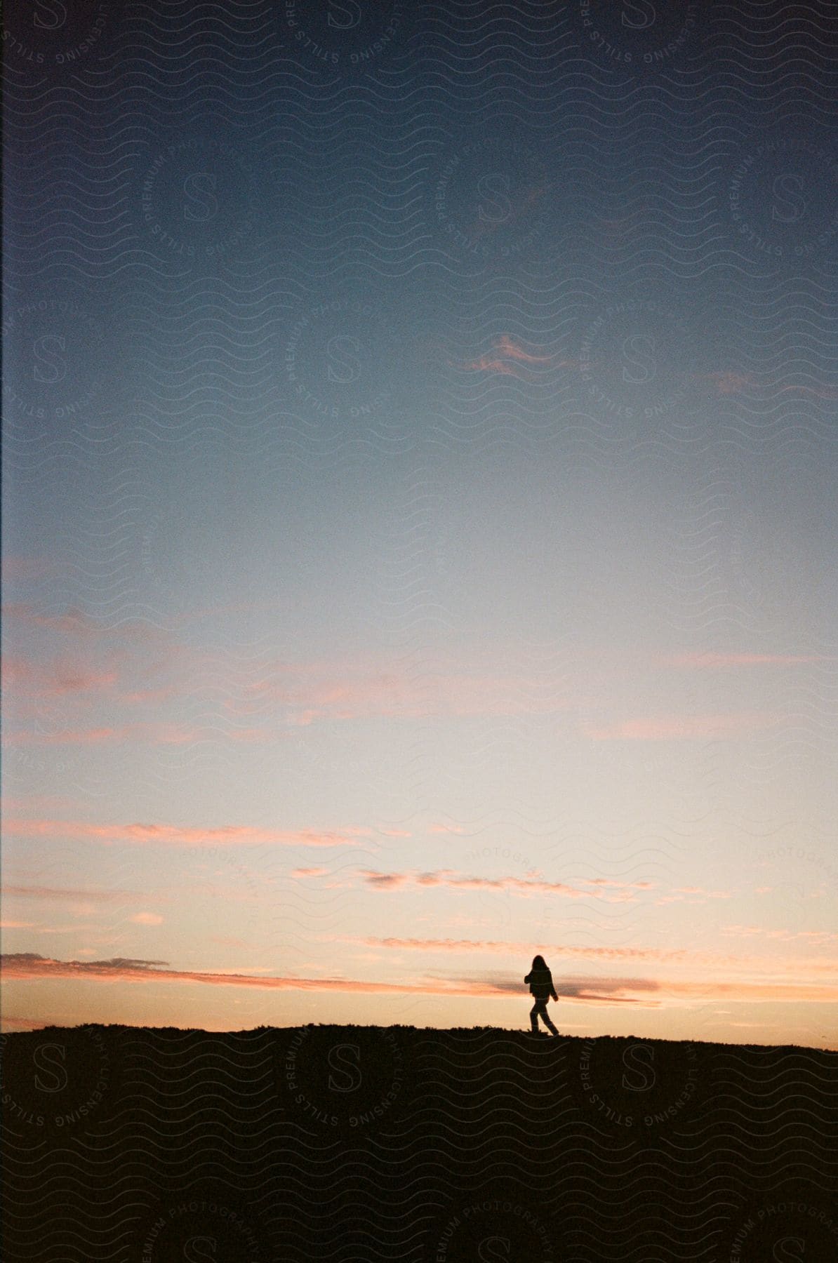 Silhouette of a person walking across the grass as afterglow reflects on the clouds