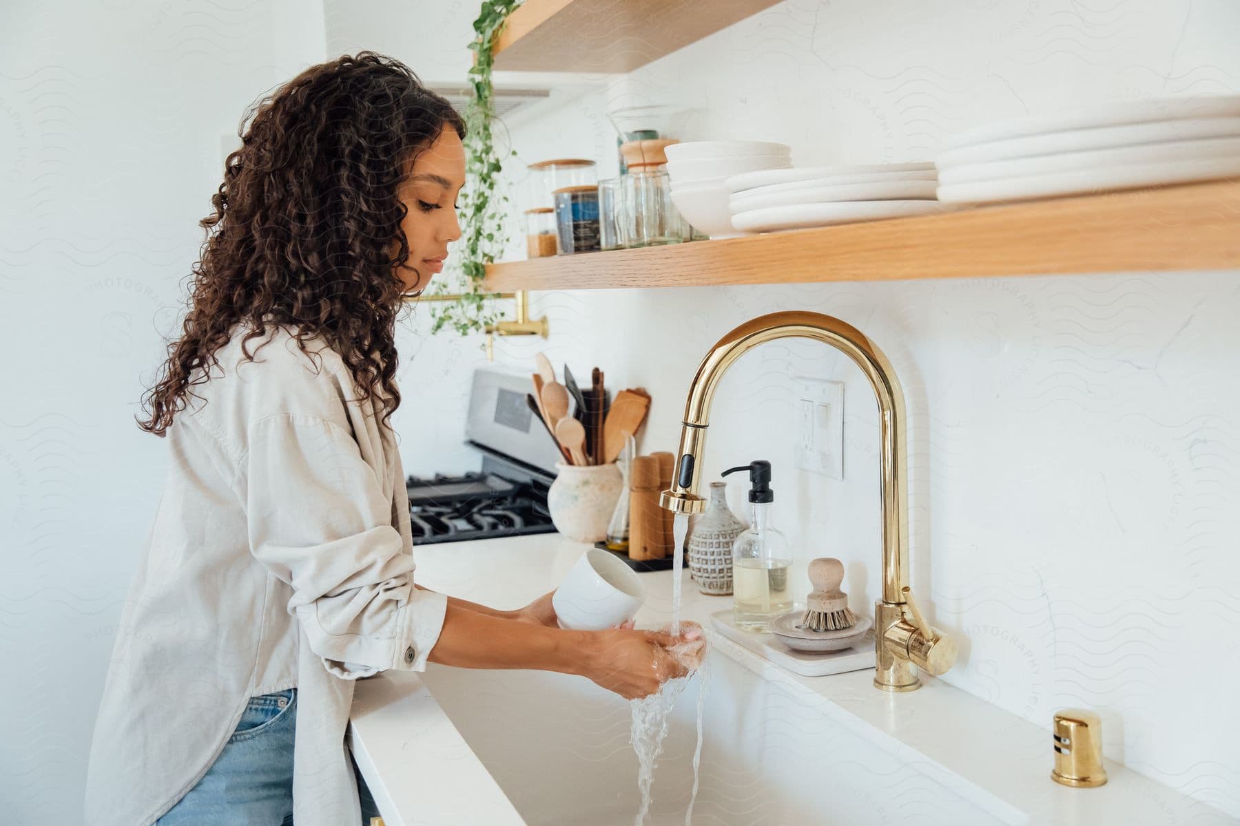 a woman inside the kitchen washing a mug in the kitchen sink