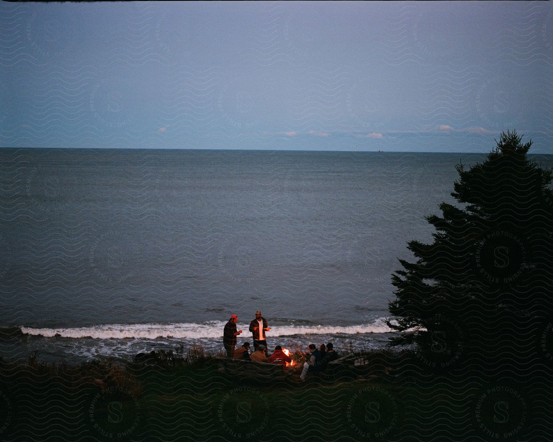 A group of people hanging out on a beach having a bonfire.