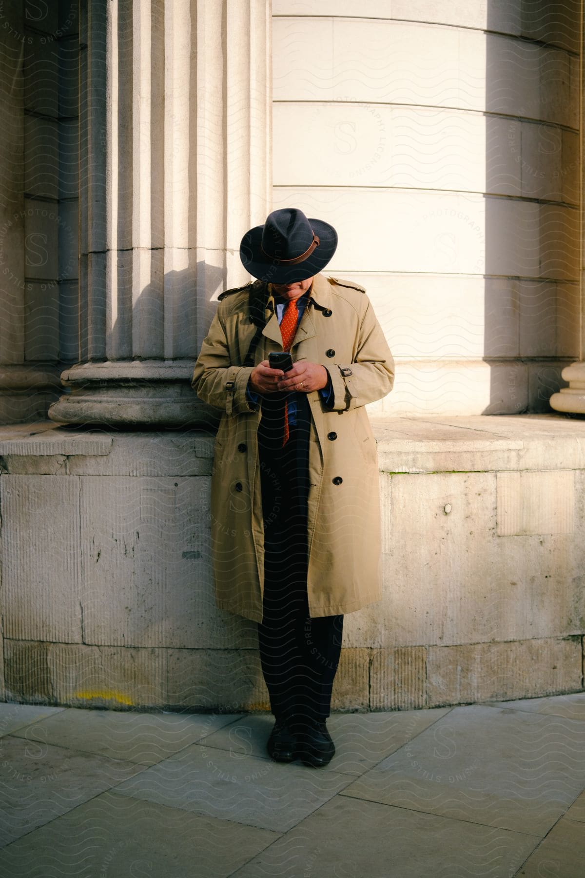 Man In A Hat And Long Coat Using His Cell Phone Outdoors