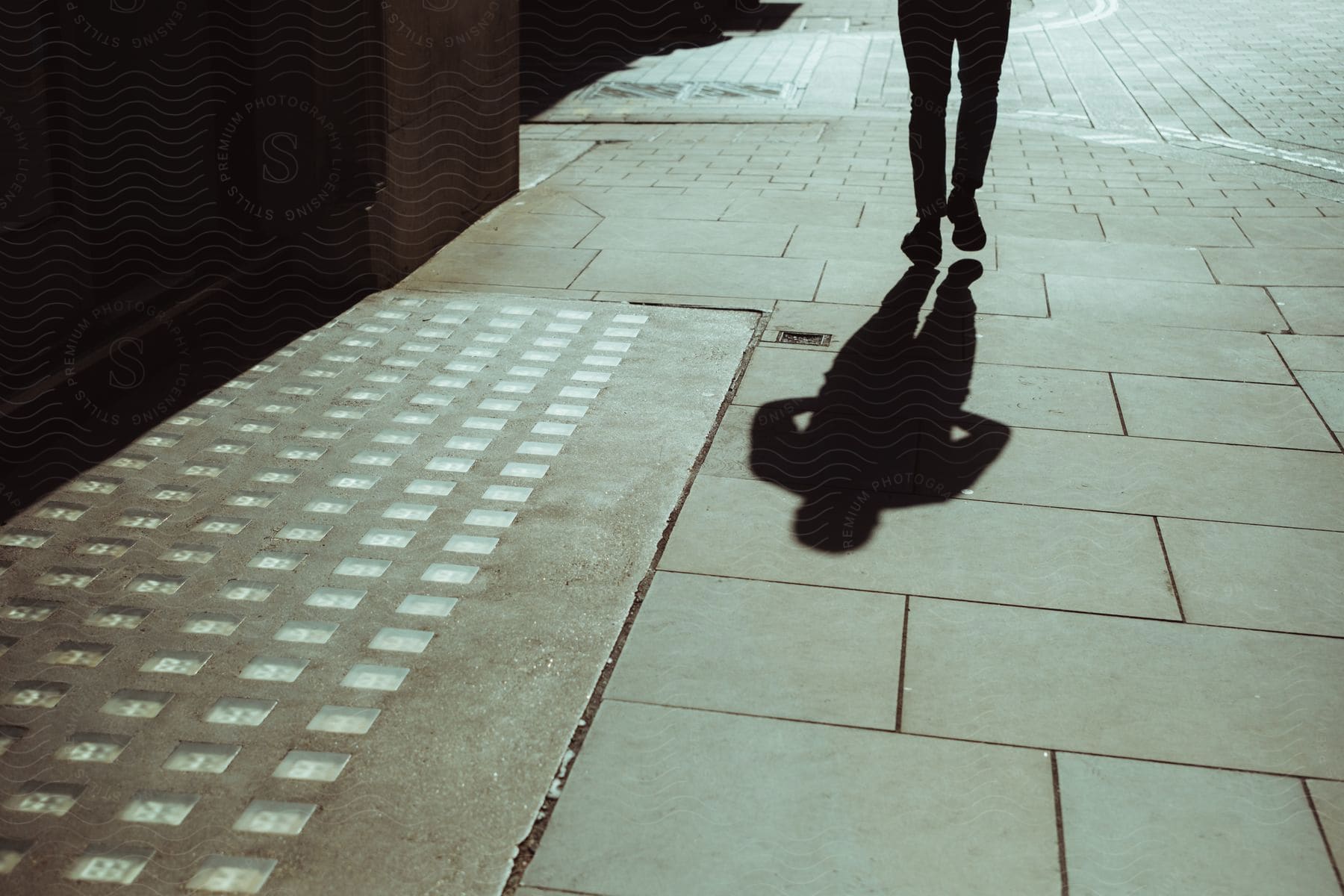 Shadow of a person walking on the surface of the sidewalk.