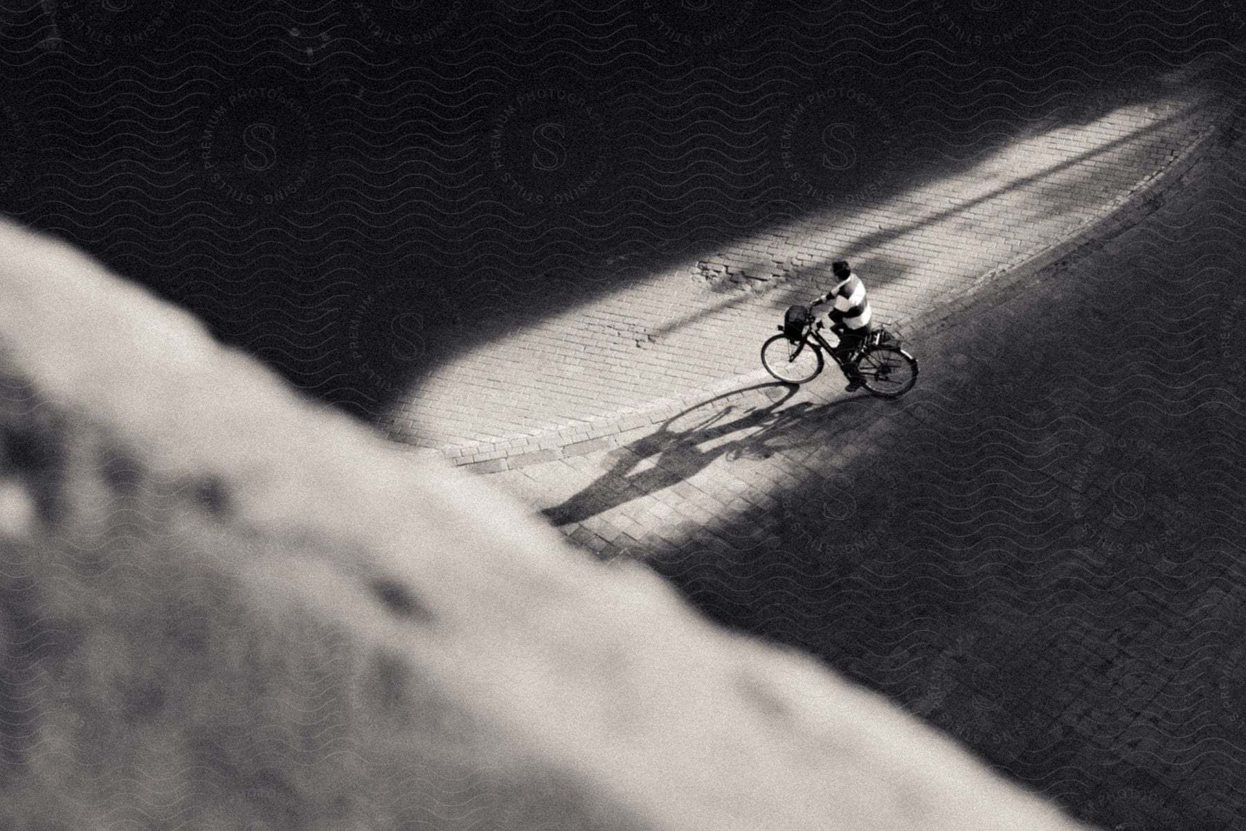 A person riding a bike in the sunlight on a cobblestone road