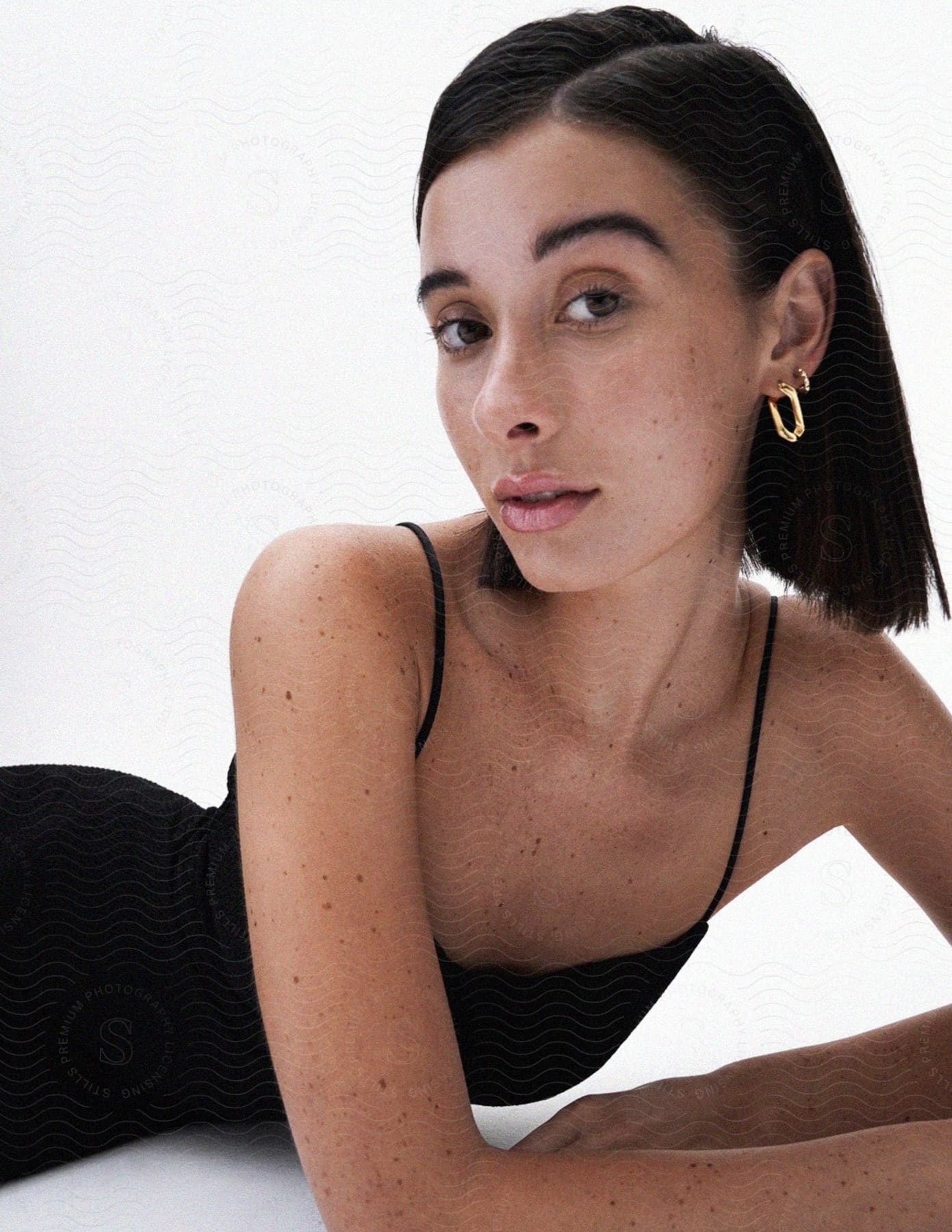 A model posed lying down wearing a black dress and gold earring