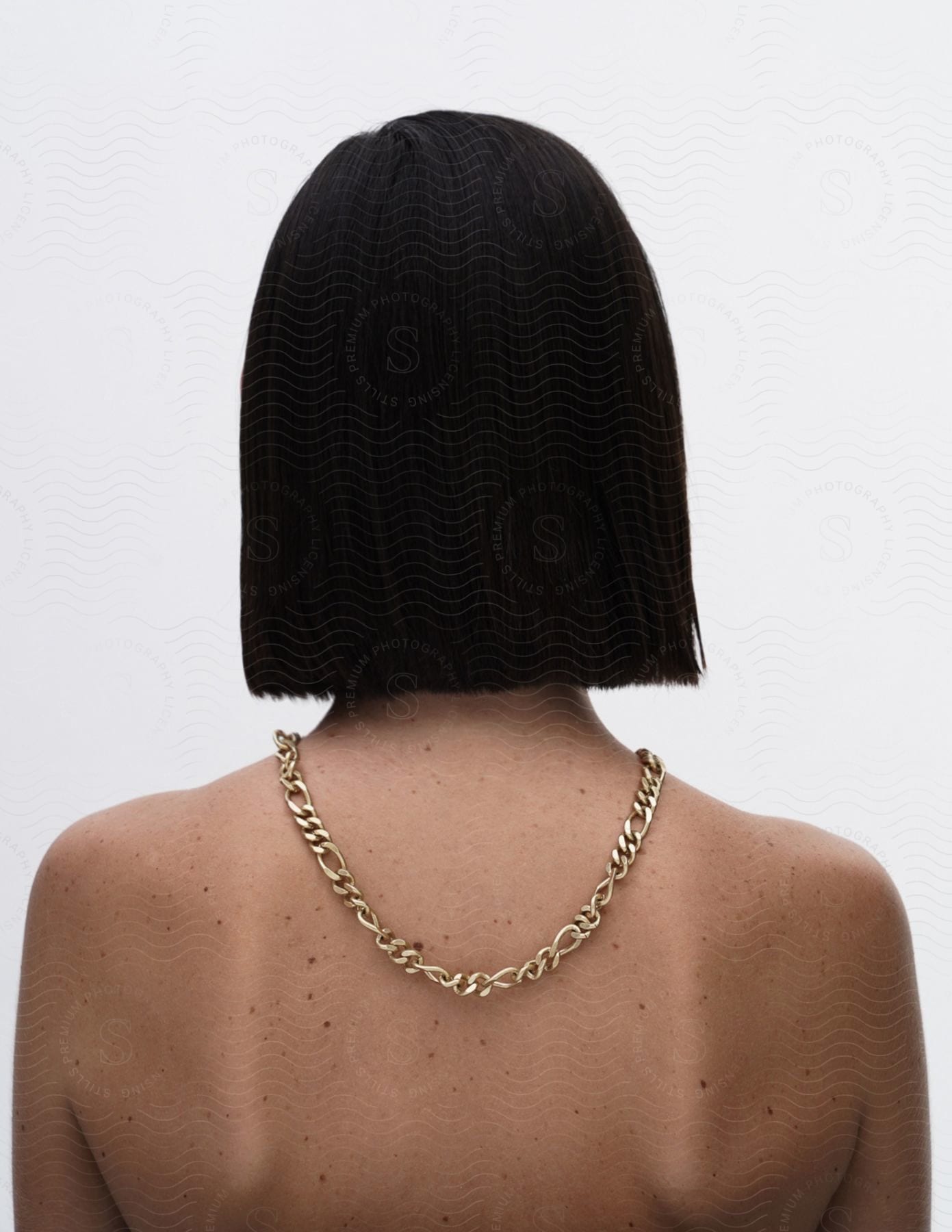 Woman standing with her back turned and black hair cut straight with a gold necklace on her back