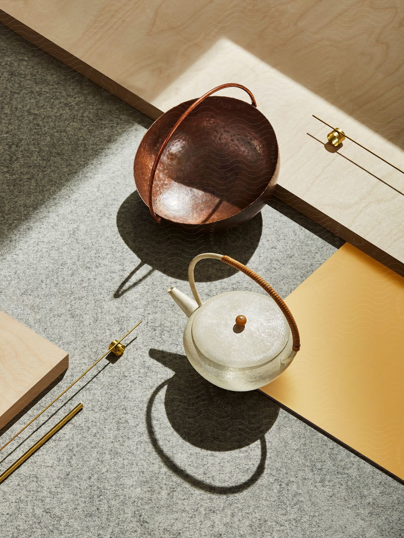 Copper bowl and white teapot with wood handle on carpet, wooden surface, and yellow accent