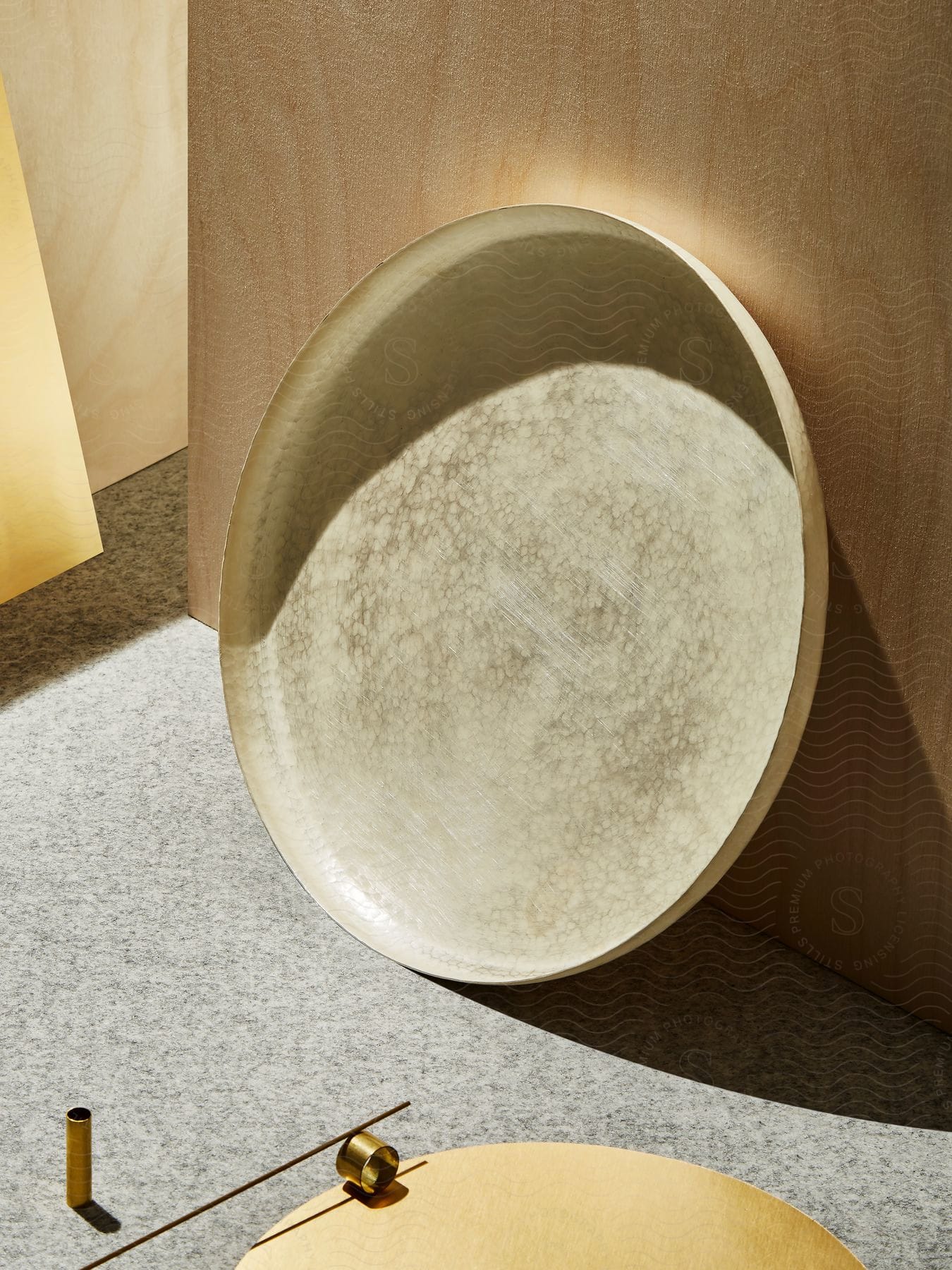 A beige circular tray is leaned upright while two small metal casings are on the floor nearby.