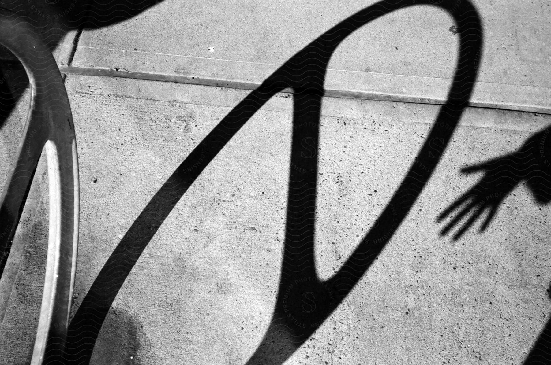 Shadow of a person's hand near the shadow of a wheel on the sidewalk