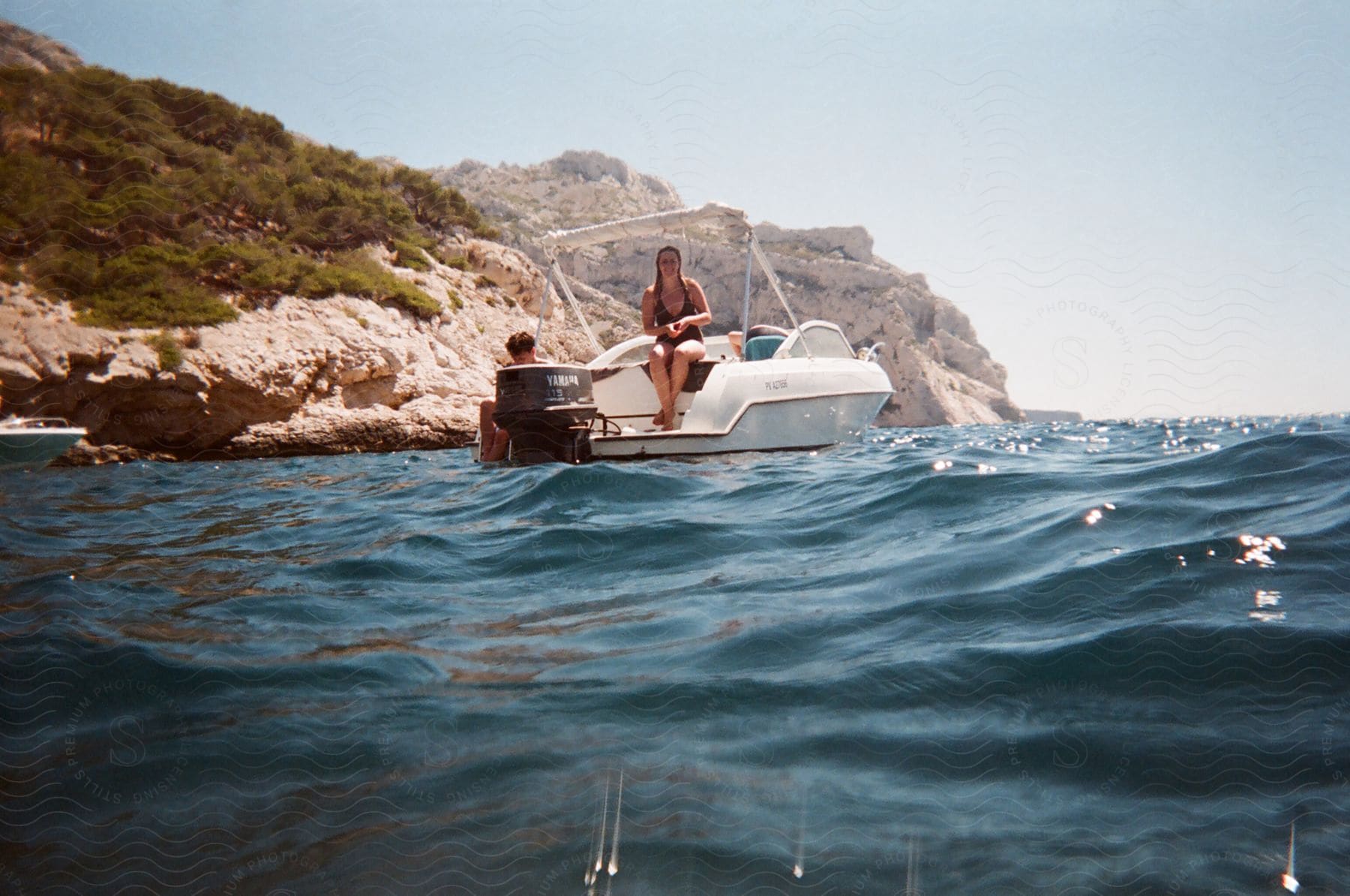 A woman in swimwear sitting on a boat near a rocky coastline