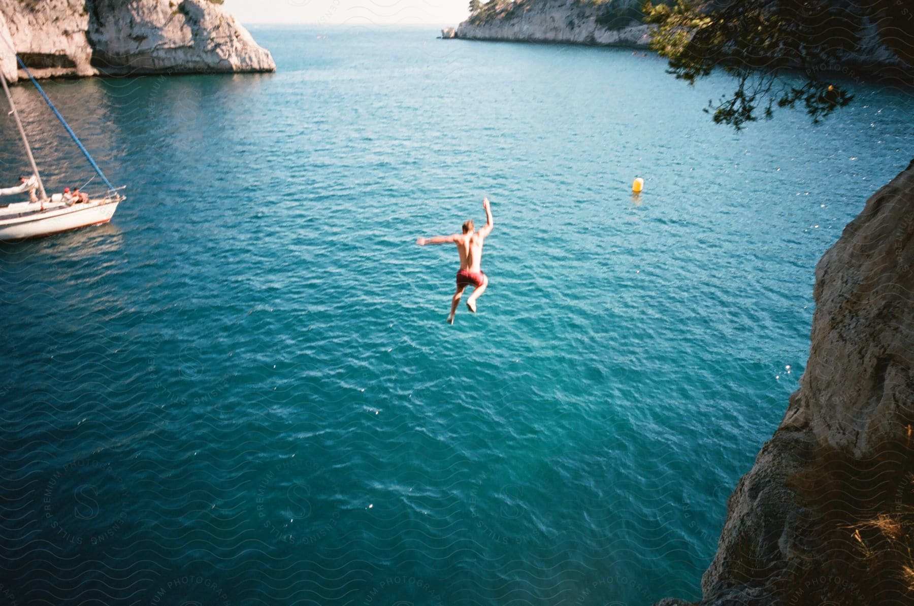 A male in swimming trunks takes a daring leap off of a cliff into the water below.