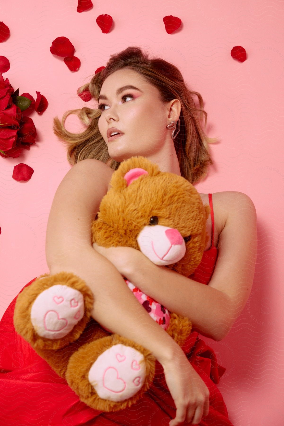 A beautiful woman hugging a teddy bear surrounded by rose petals