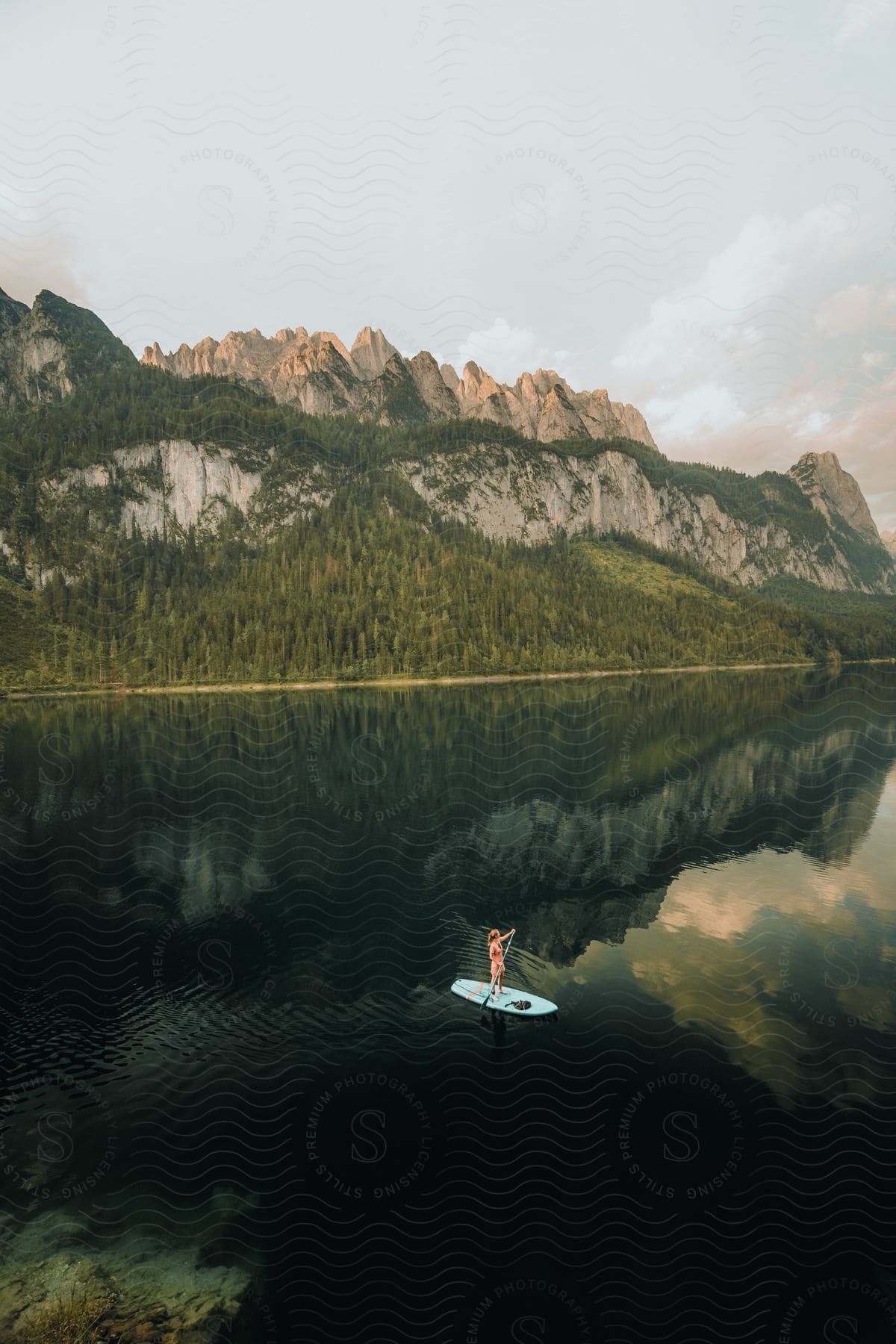 Woman paddleboarding on calm lake with forested mountain reflection in the water