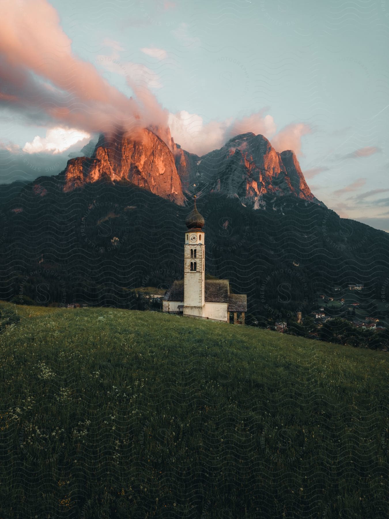 A rural church sits on a hill near a mountain overlooking a village.