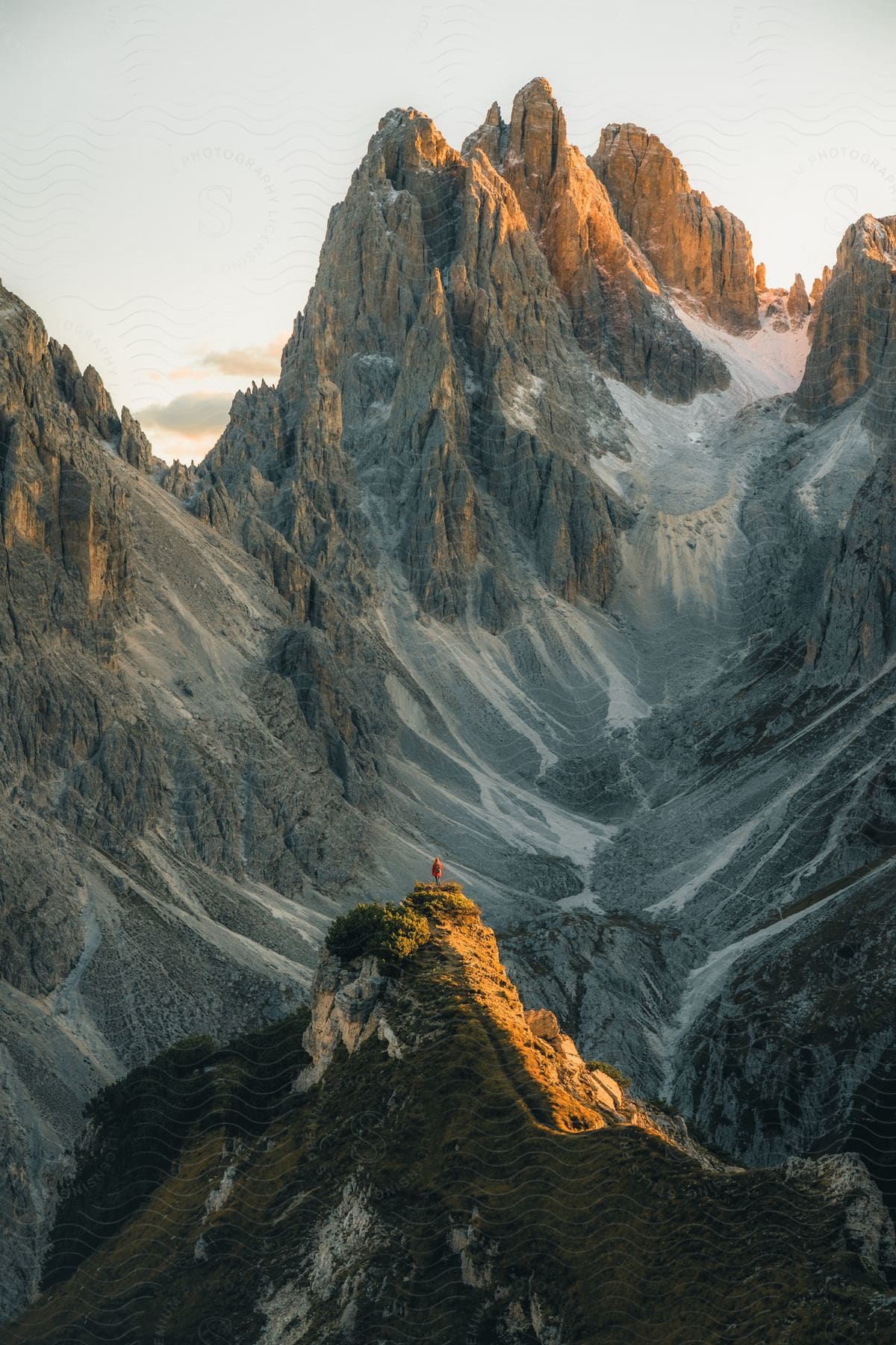 A man stands on a point of rock looking out over huge rocky mountains.