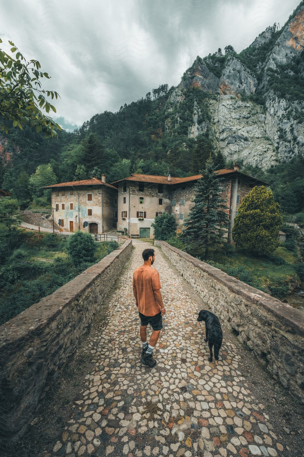 Man walking with his dog near apartment buildings along a mountain cliff outside of the woods