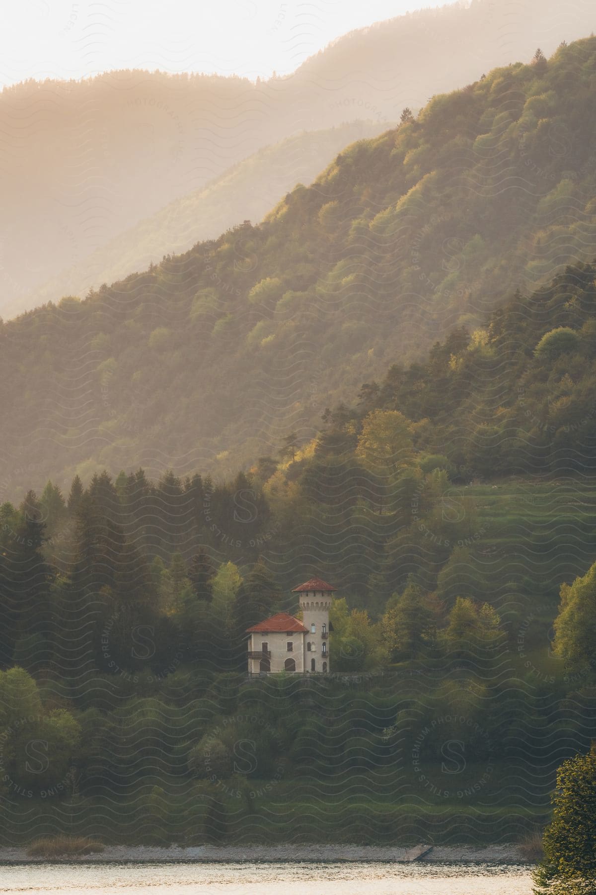 Small castle sits at the foot of a forested mountain along the coast under a foggy sky