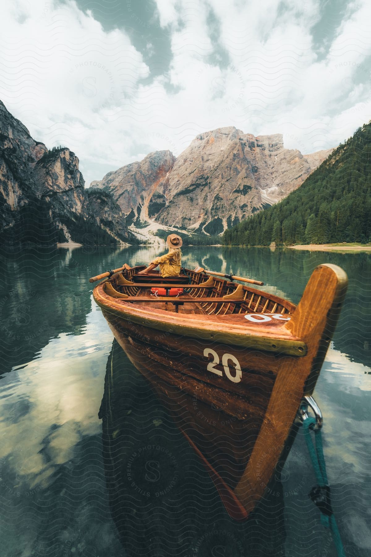 Lake with a canoe and a woman sitting with a beautiful view of mountains and conifers around