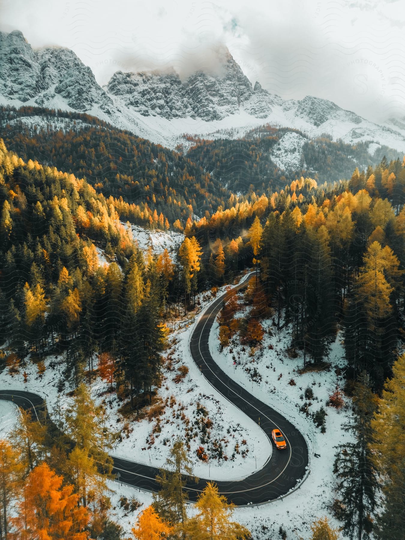 Aerial panorama of a road around mountains and conifers covered by snow on a cloudy day