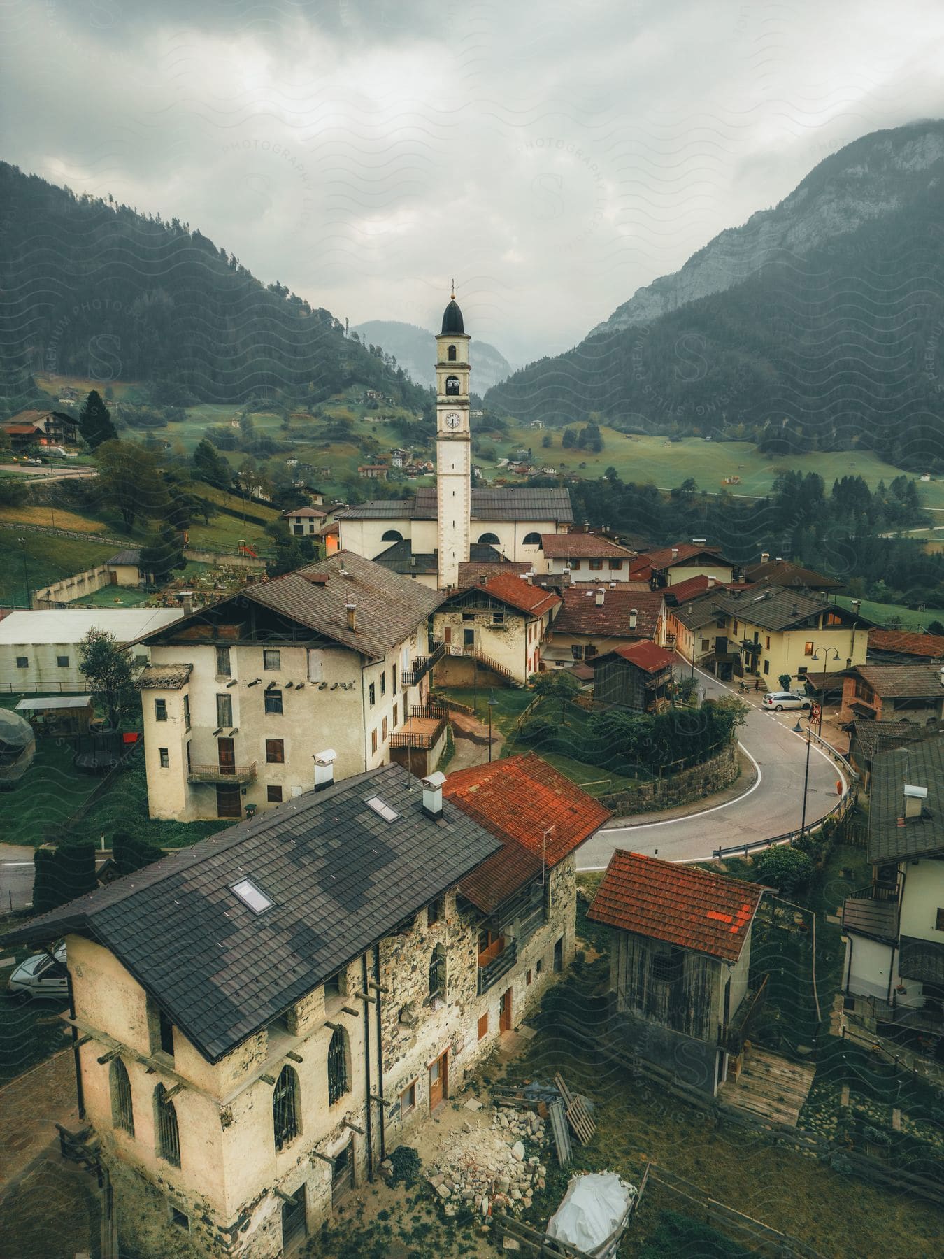 A bell tower sits in the middle of a small mountain village on a cloudy, summer day.