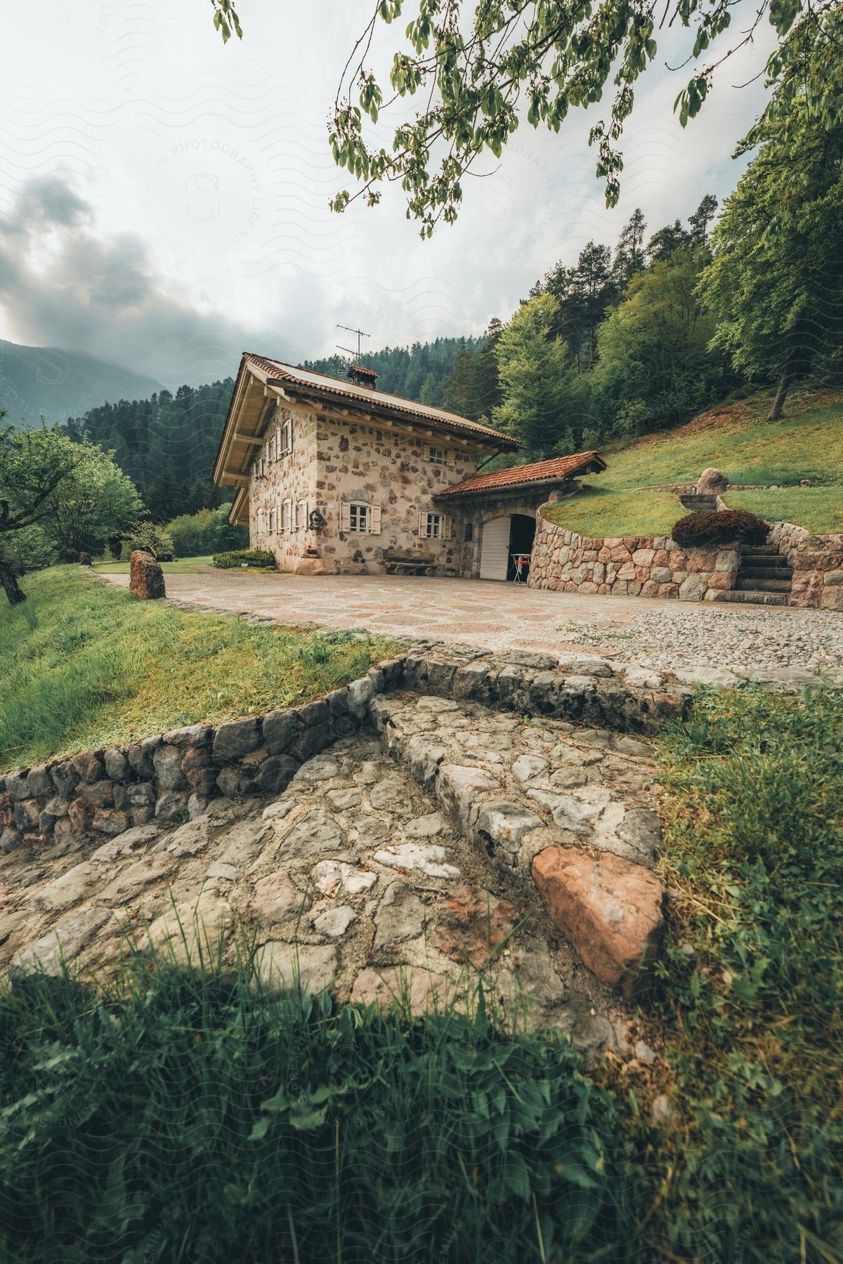 House along a rural hillside road leading to forested mountains in the distance