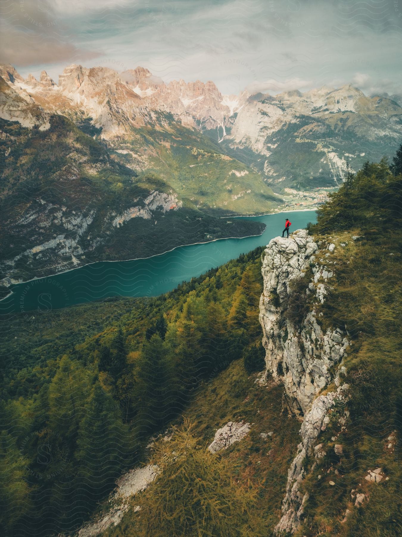 A man stands on the edge of a cliff overlooking a river running past rocky mountains.