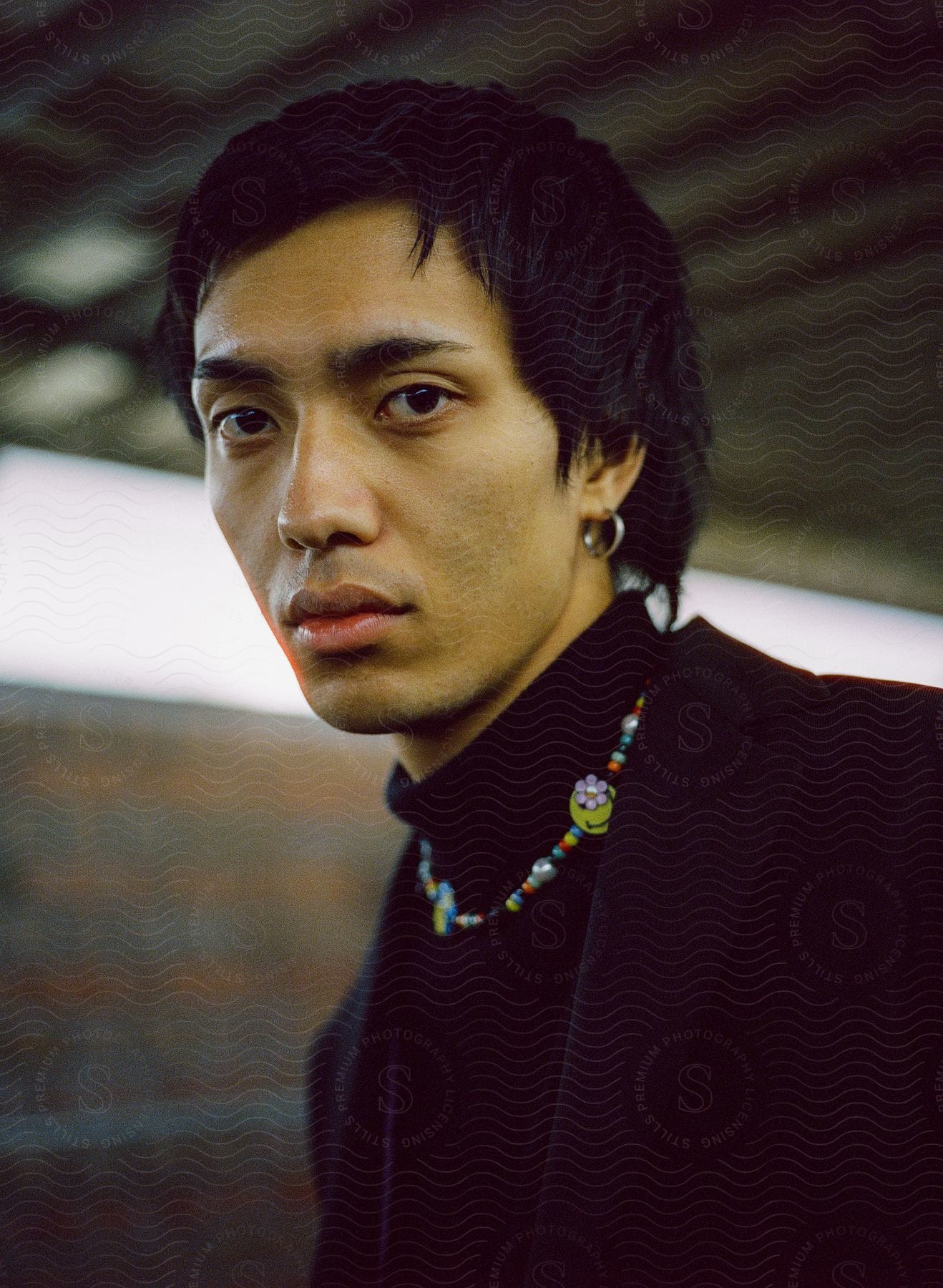 An Asian man wears a colorful necklace and black clothing.