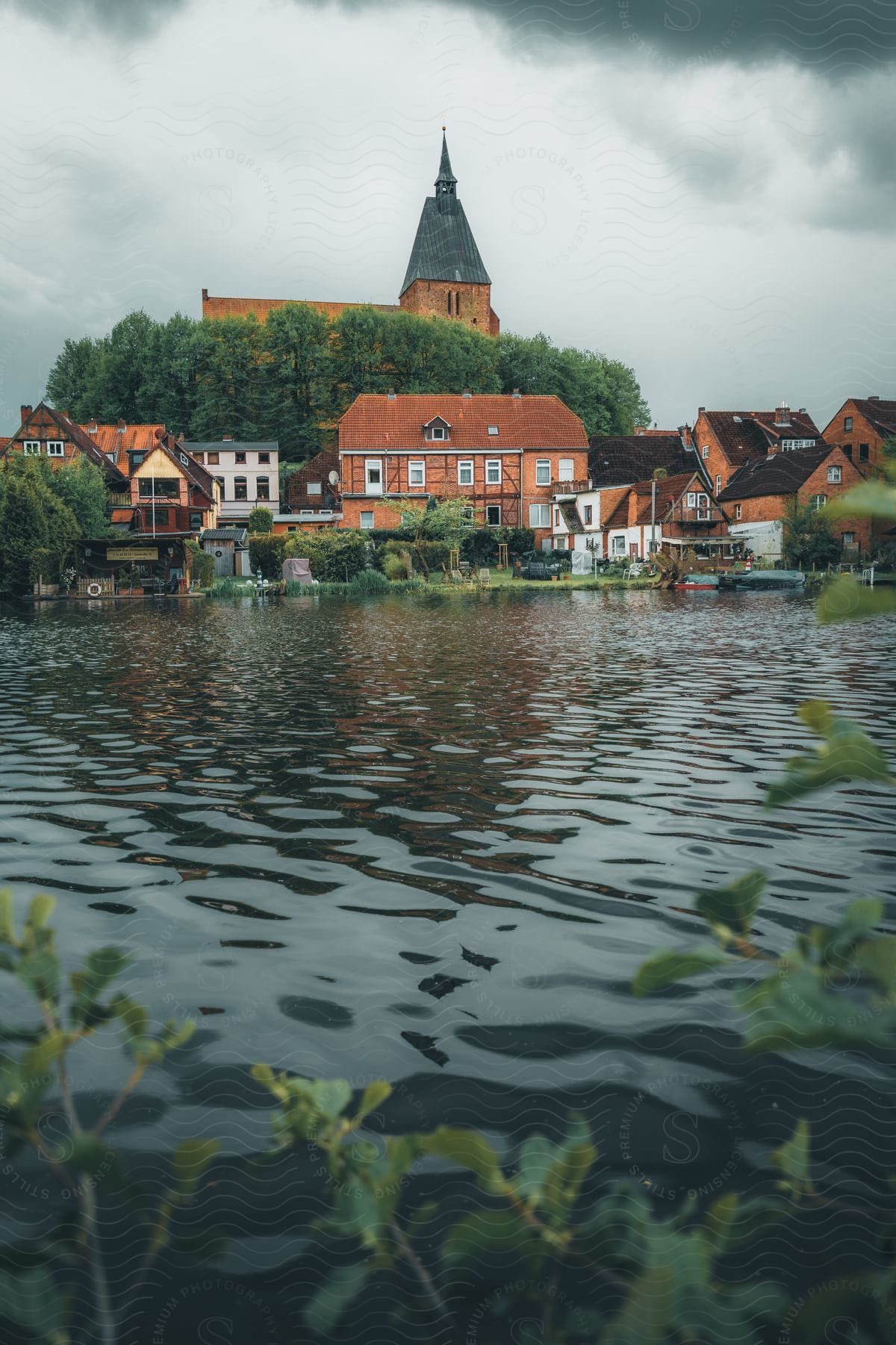 Church towers over nearby buildings in waterfront town under a cloudy sky.