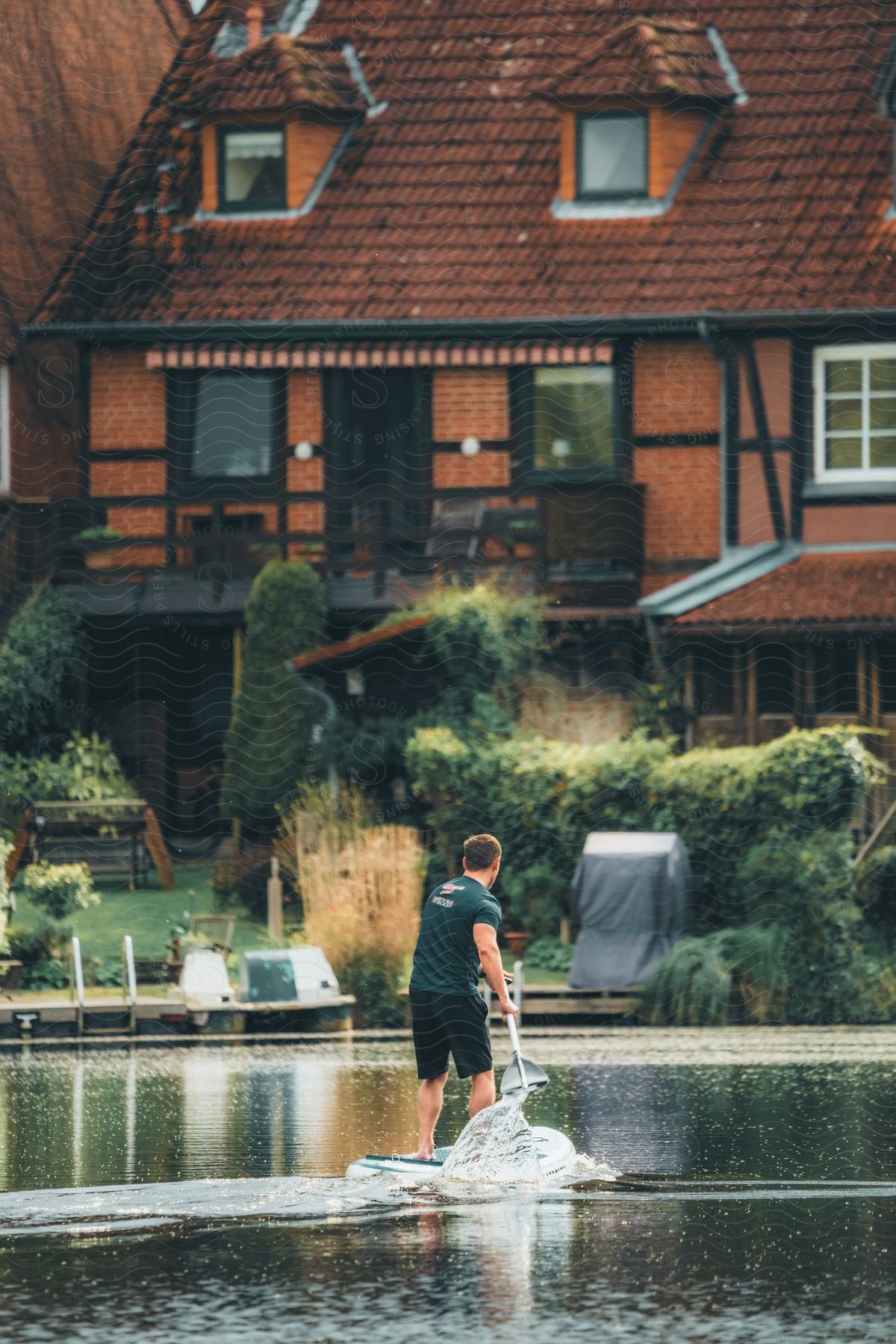 A man standup paddleboards with brick buildings in the background.