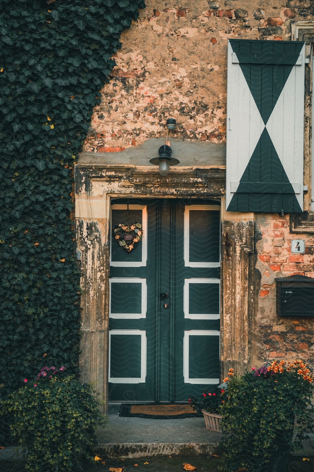 A green door with a white trim and a green and white window shutter are on a rocky wall.