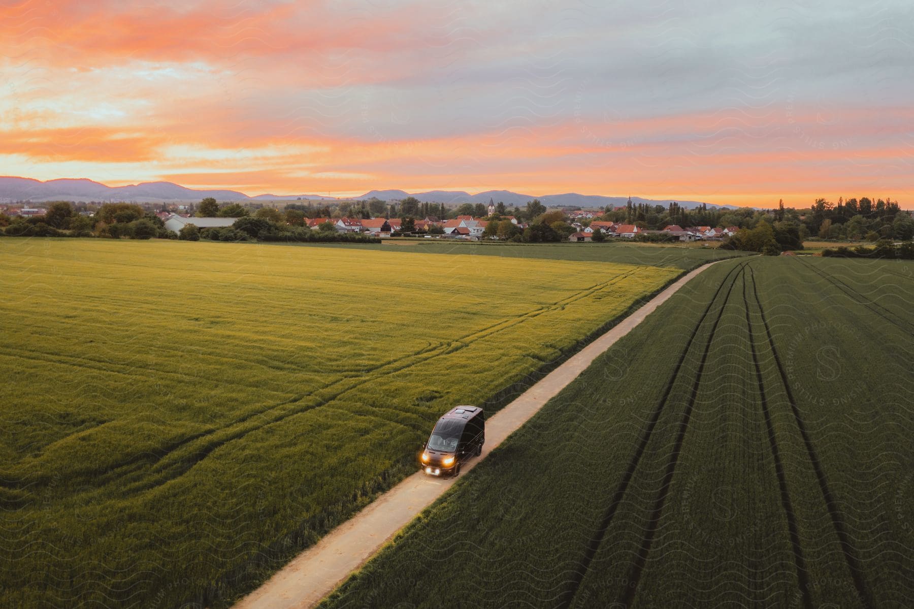 a black van driving out of a small town at sunset with plain green grasses surrounding the road on each side