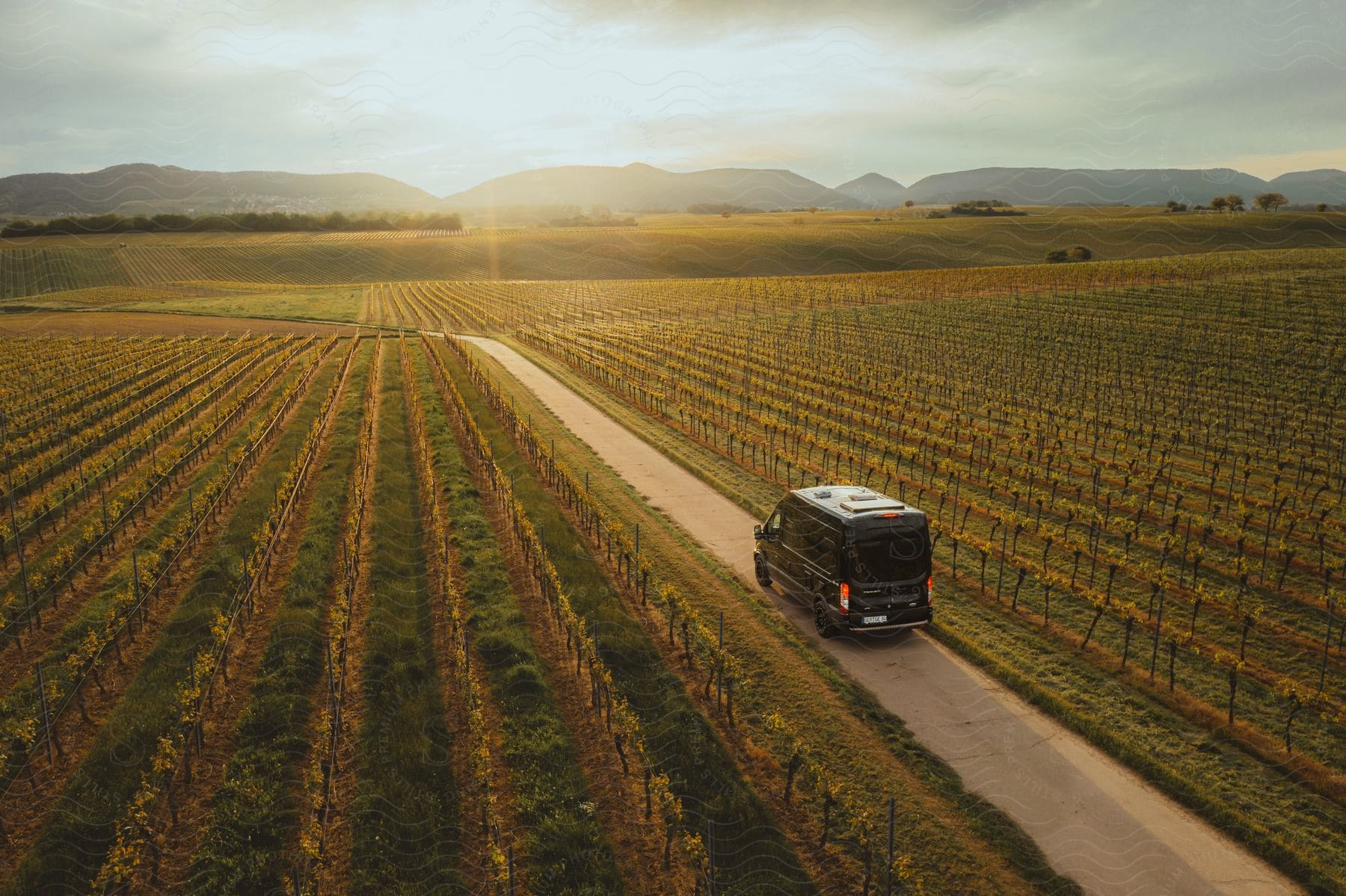 Black van on country road by field at sunset.