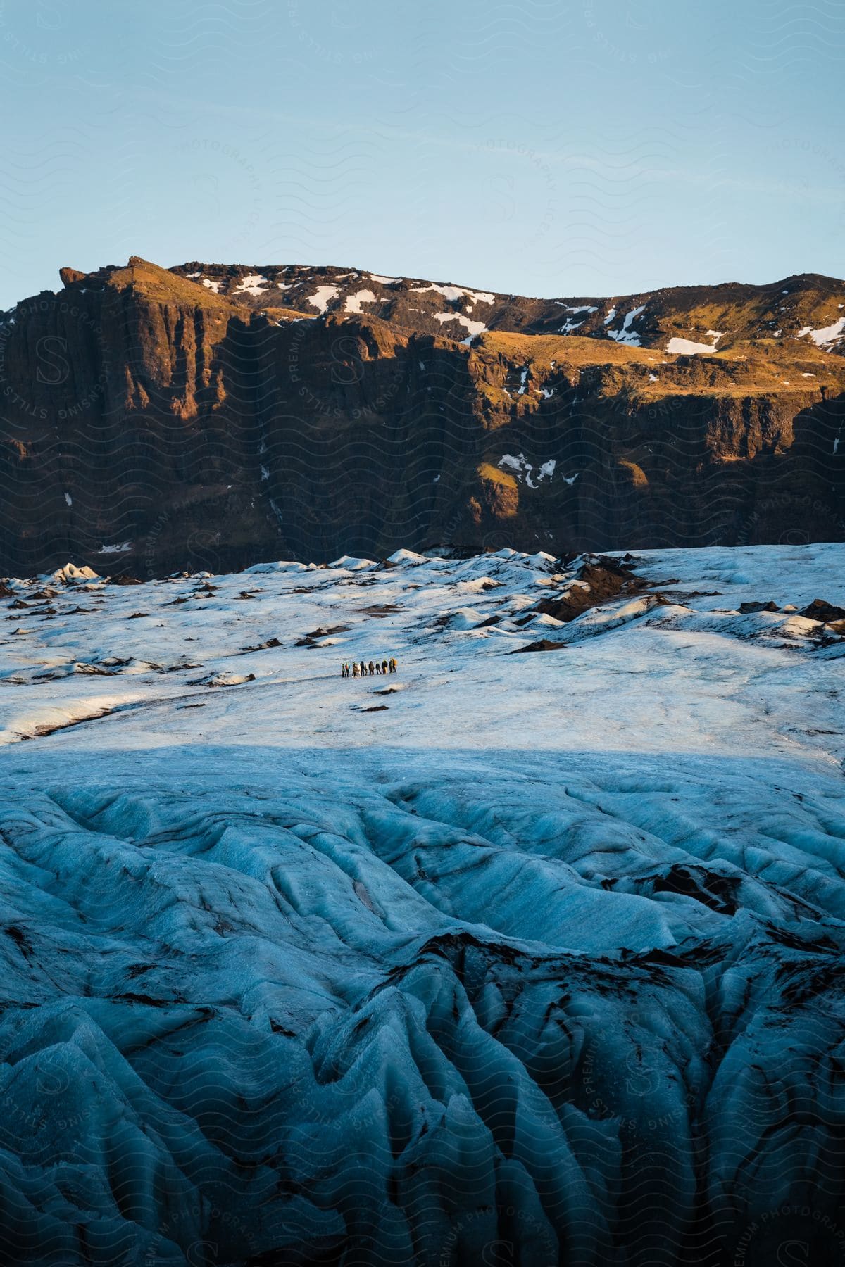 A group of people hiking across a glacier below steep cliffs.