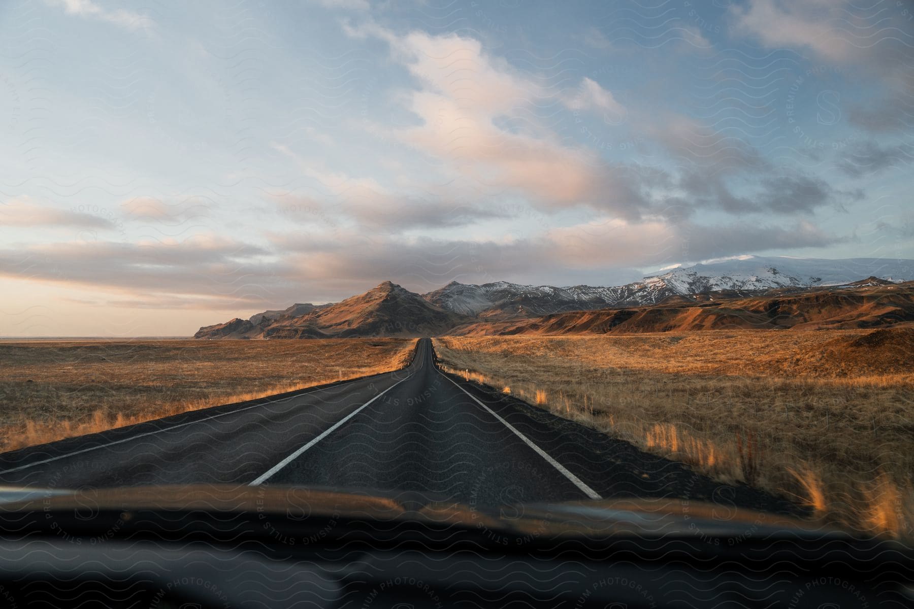 A road runs through brown grasslands towards a snowy mountain range.