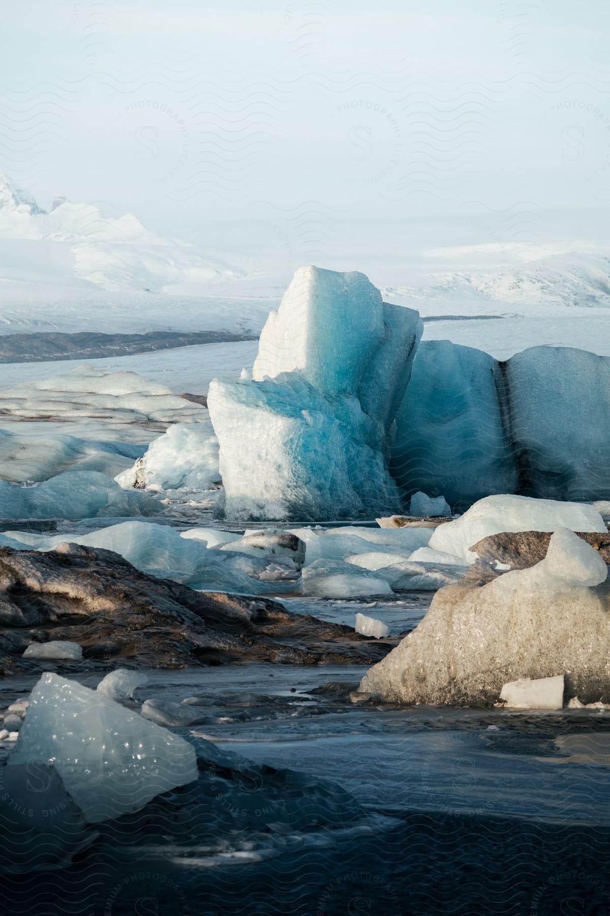 Glacial ice formations among meltwater with snow-covered mountains in the distance.