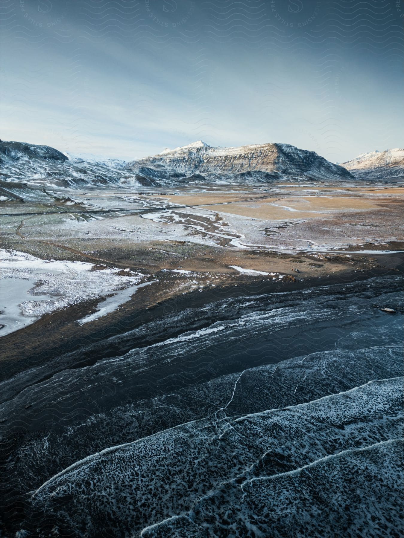 Aerial of a beach with flat, snow-capped mountains during winter.