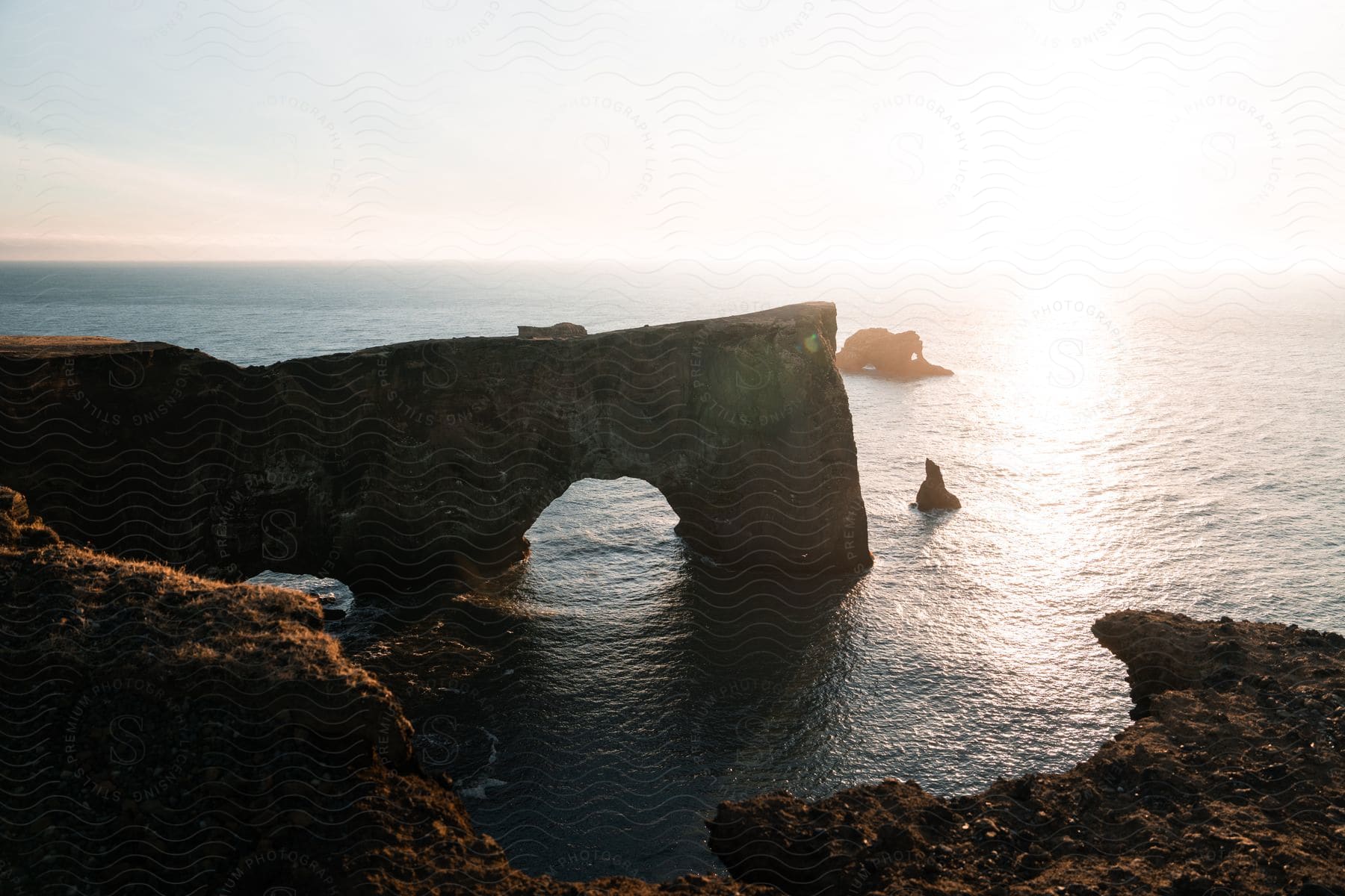 Natural rock arch on coastal cliff with ocean and sunset in the background.