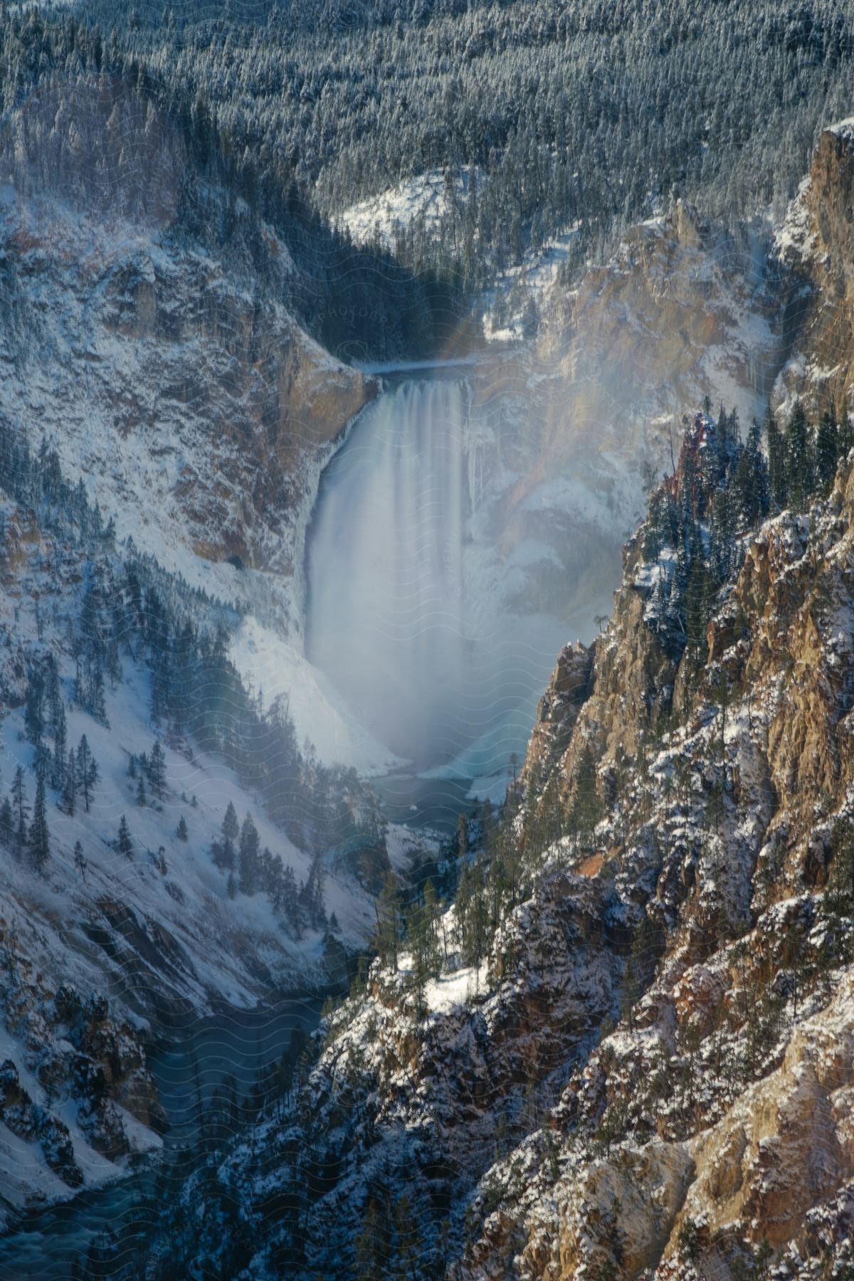 Stock photo of snow-covered trees line a mountainside, with a distant waterfall cascading down.