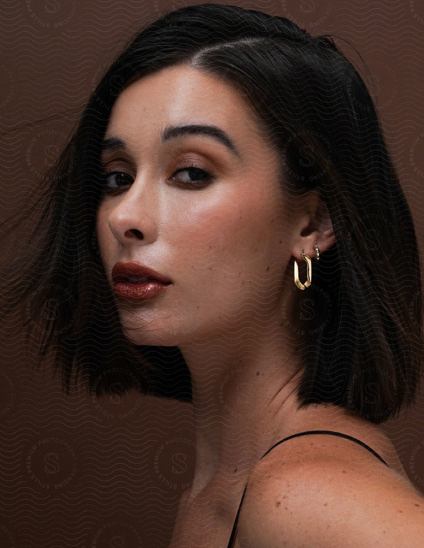 Stock photo of woman with short hair and hoop earring against a brown background.