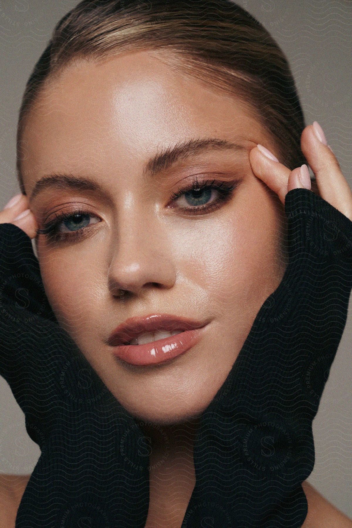 A woman models her makeup with her hands framing her face