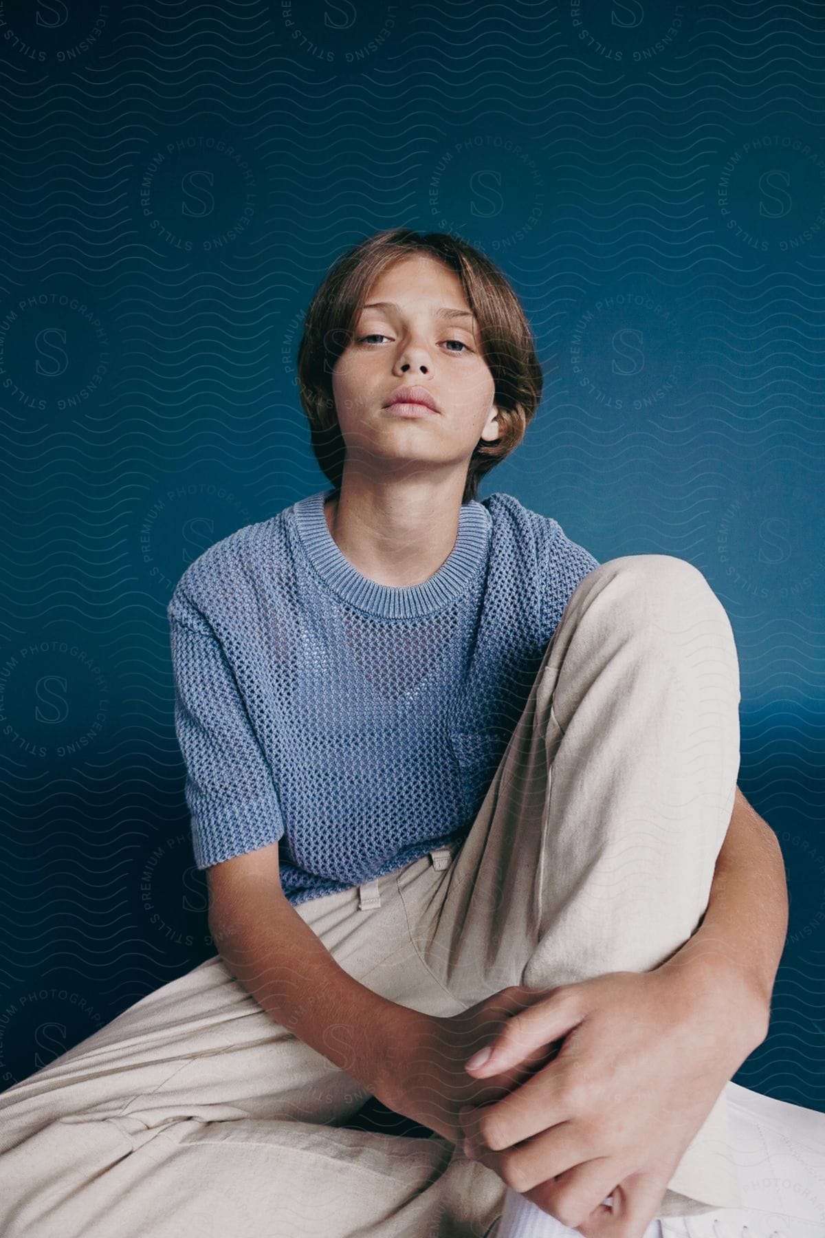 Little boy sitting in a studio posing in beige pants and a blue t-shirt