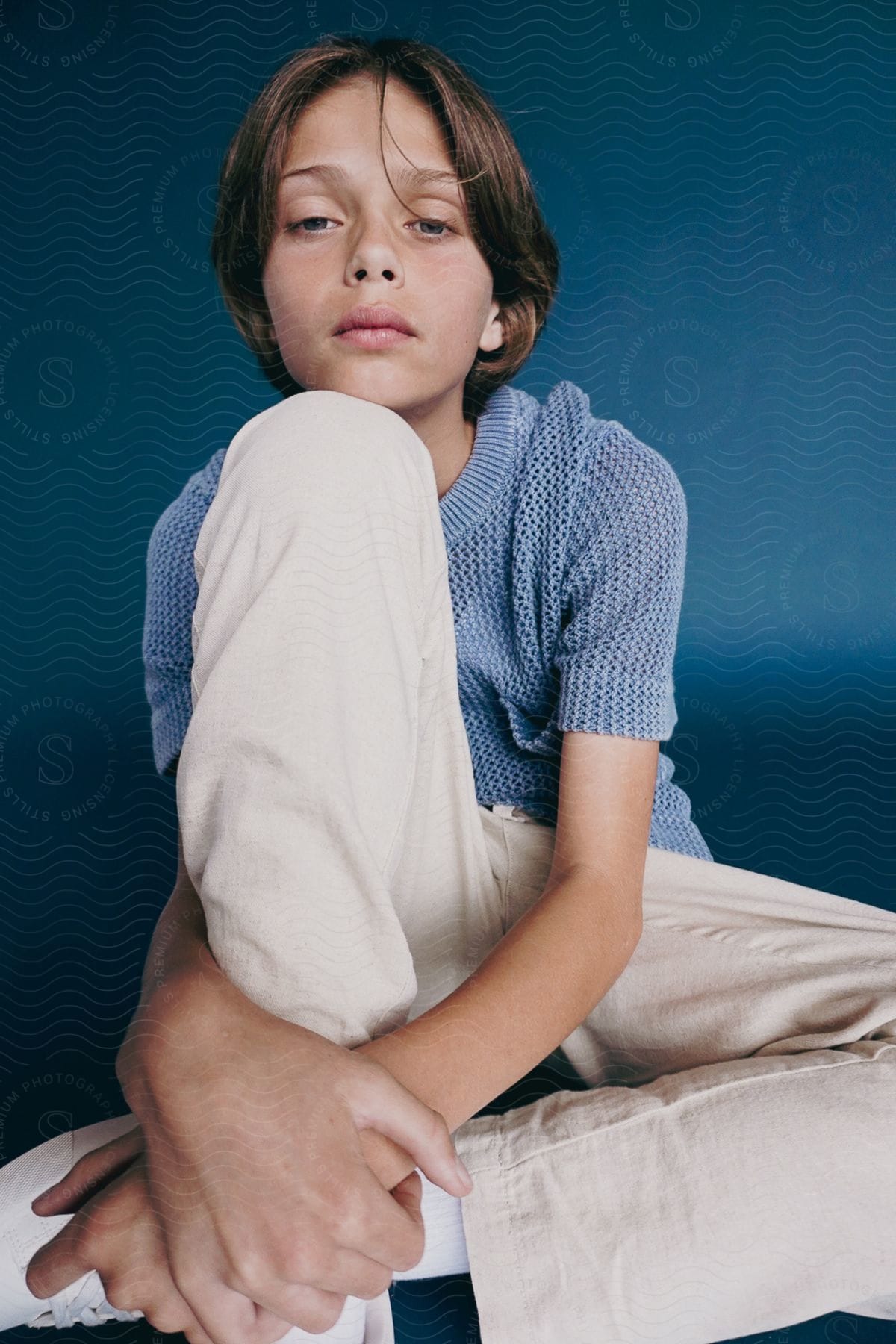 A portrait of a boy siting and folding his hands around his leg