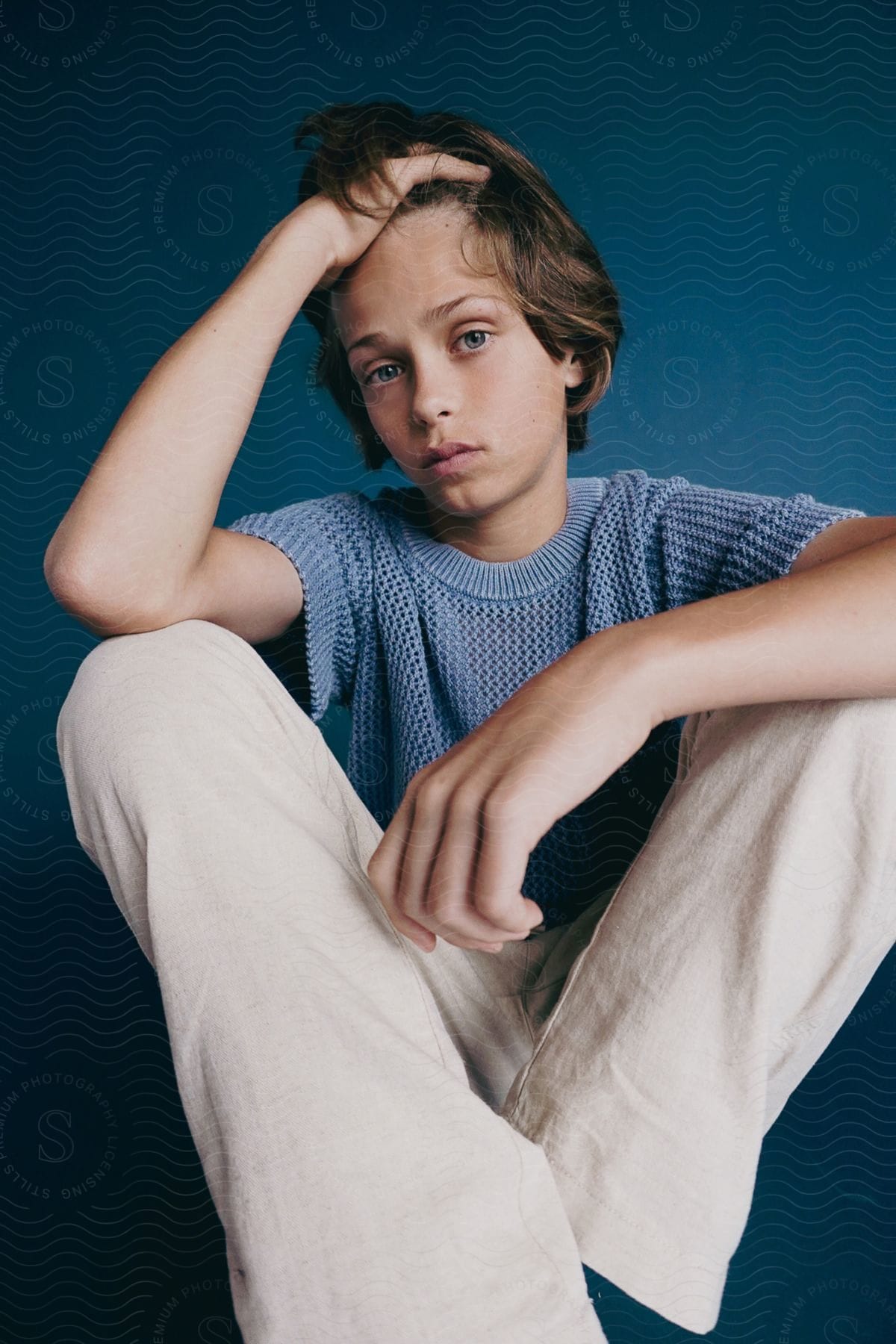 A young boy, sitting on the floor and running his hand through his hair, posing for a photo.