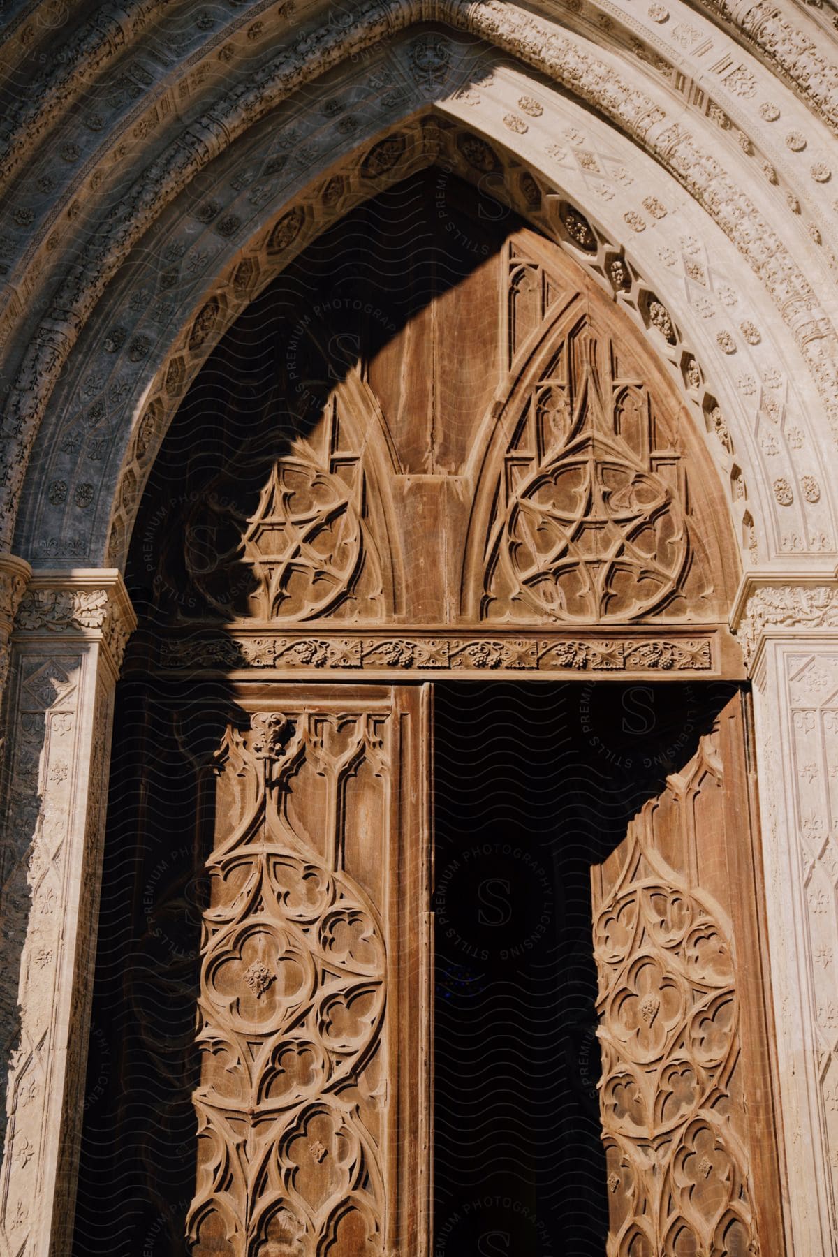 An intricately carved wooden door stands open beneath a curved stone arch.