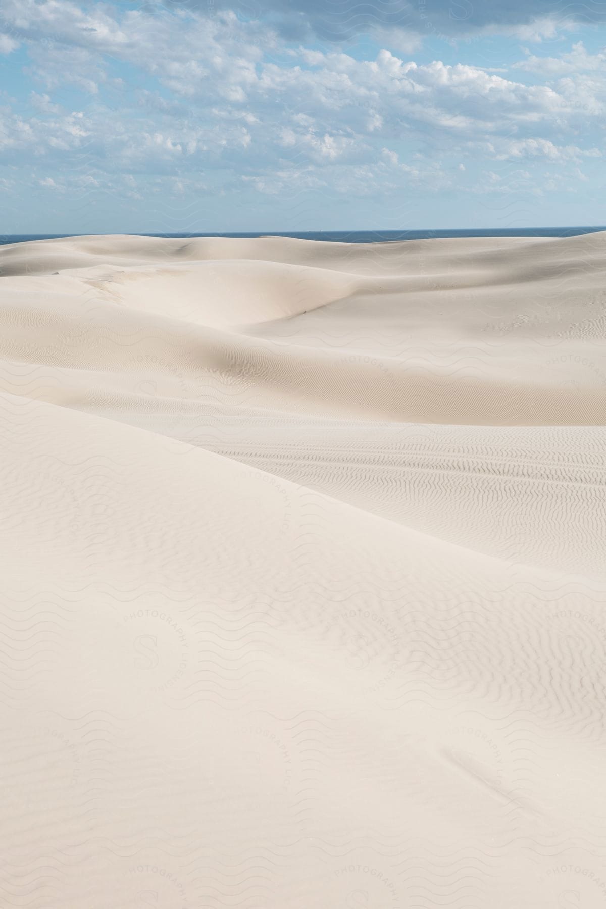 A serene view of gentle dunes beneath a sky dotted with fluffy clouds.