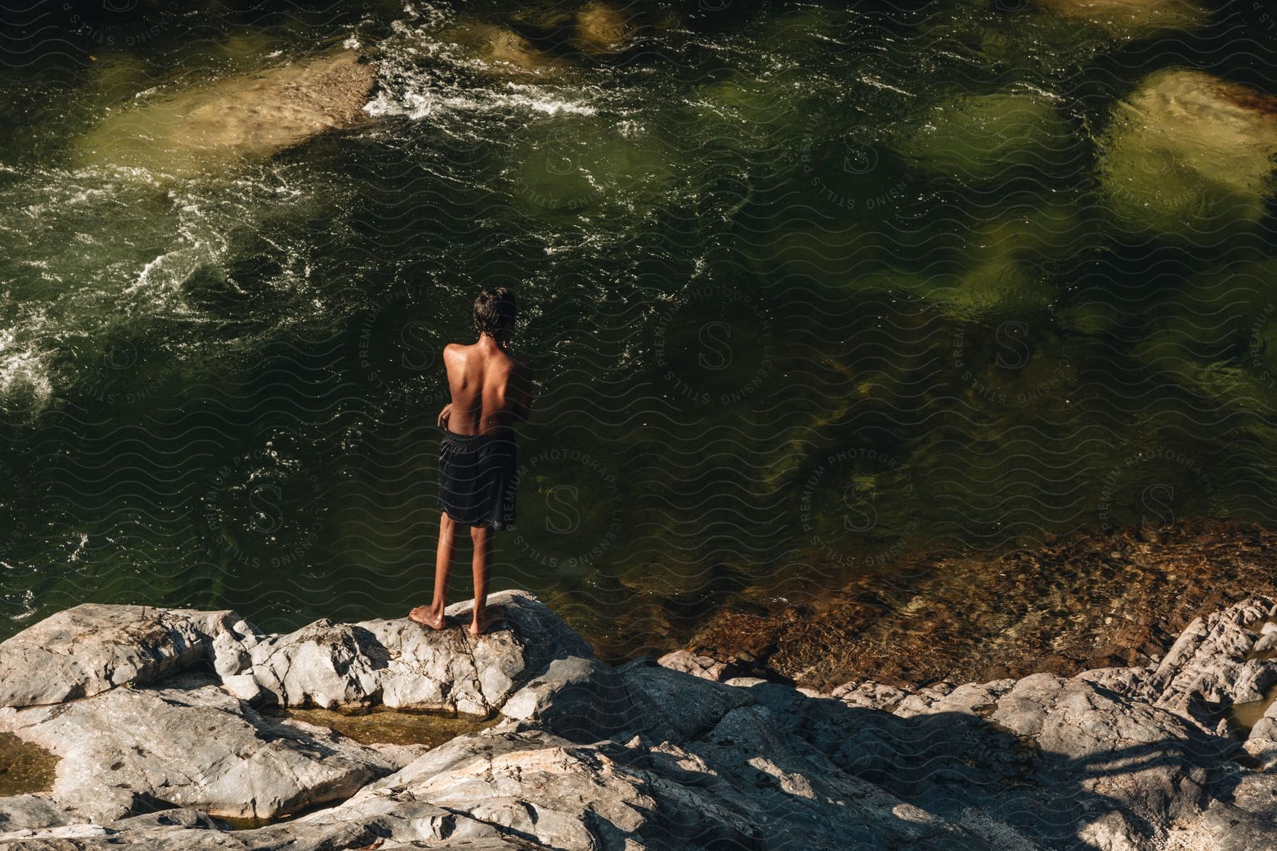 a teenager standing on the riverbank on a rock watching the flow of the water