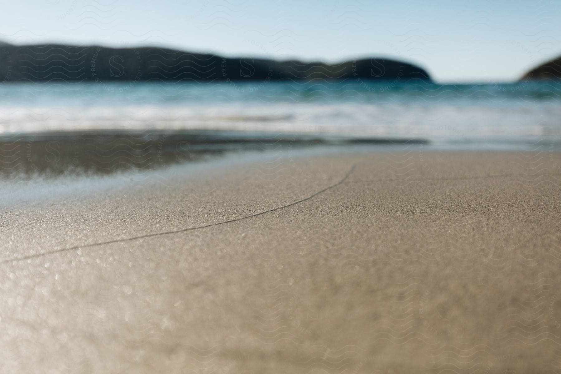 Quiet beach with smooth sand, gentle waves and hills in the background.