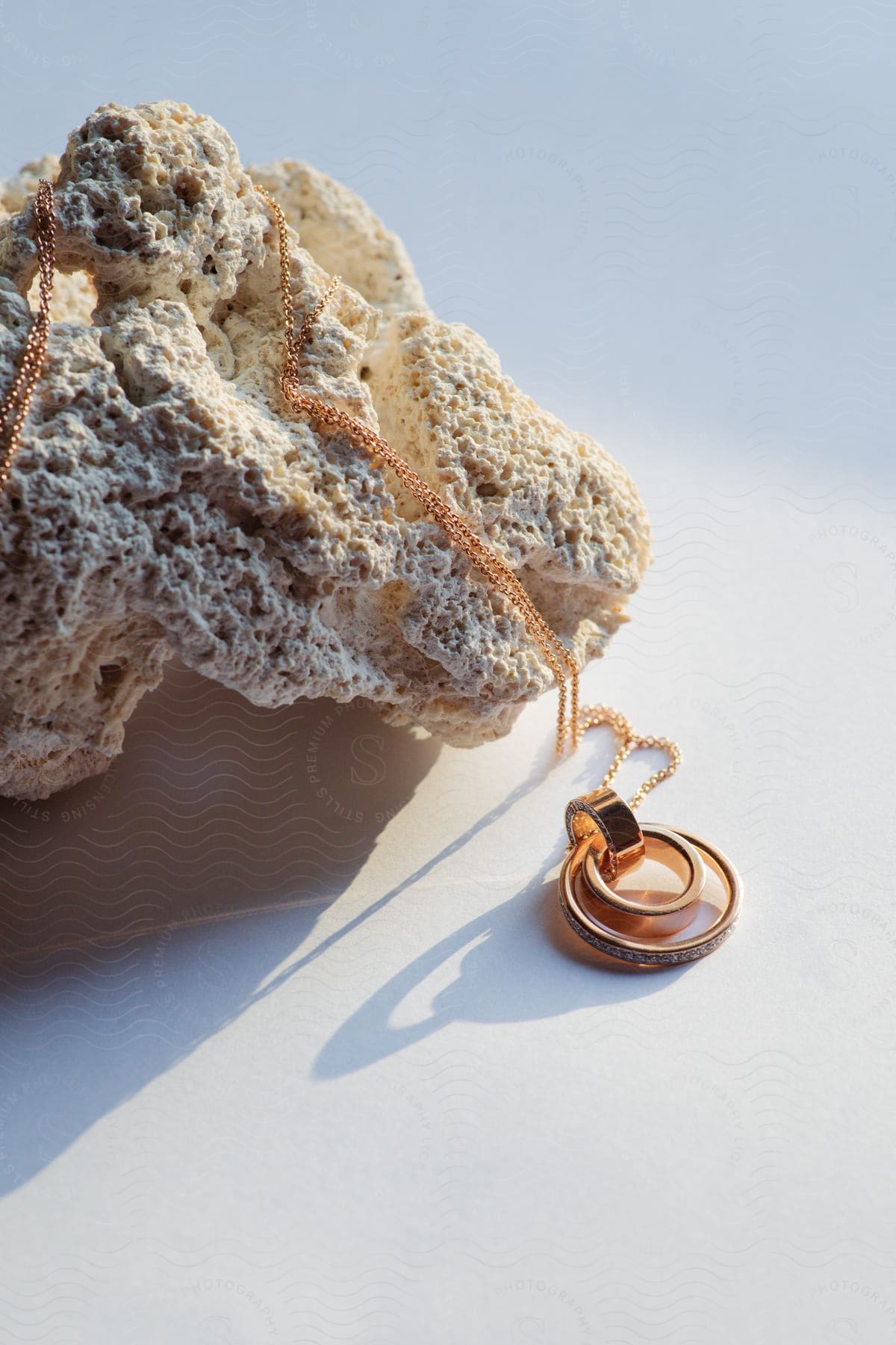 A necklace chain with rings is lying over a rock and on a white surface