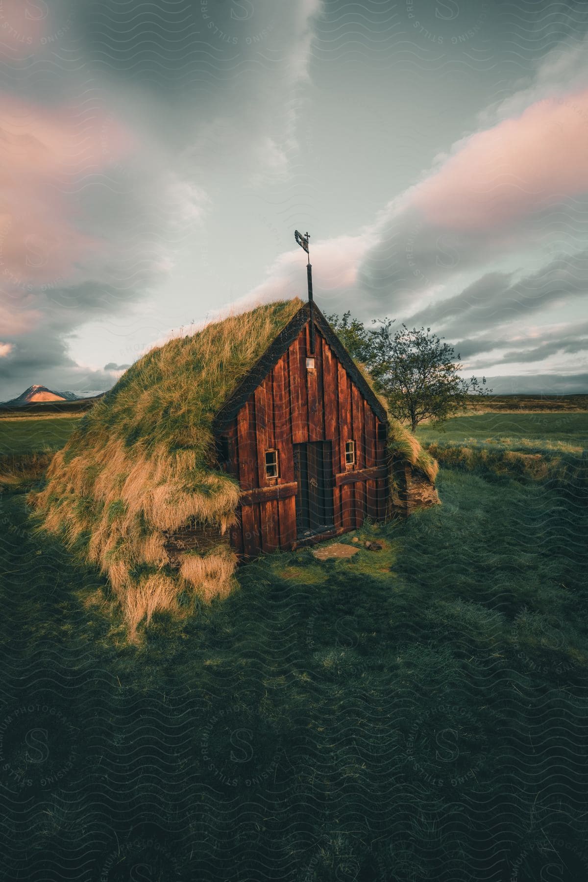 Grass-roofed wooden cabin with cloudy sky at dusk.