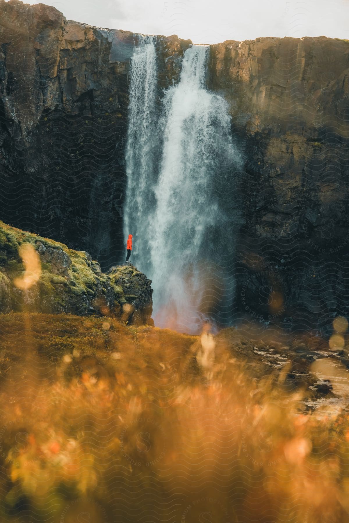 A person is standing on a rock near the waterfall as it splashes and flows down the side of a cliff