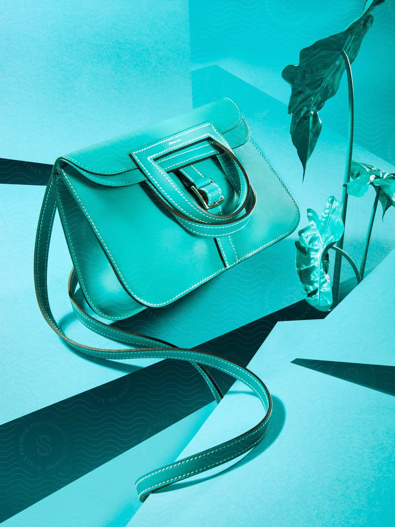 A light blue purse next to a light blue plant in an angled surface.